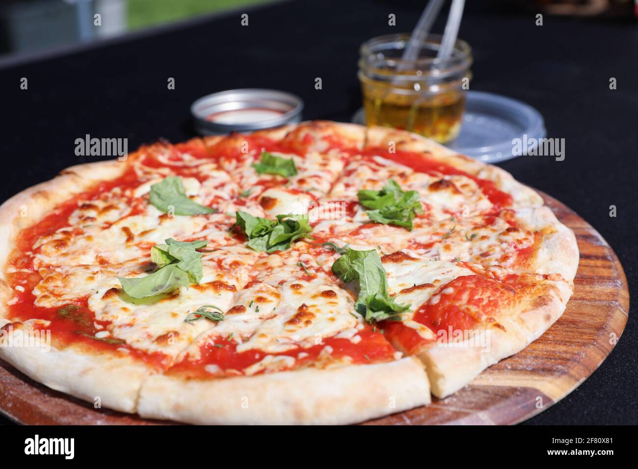 la pizza viene servita su un piatto di legno su un nero tavola con olio d'oliva sullo sfondo Foto Stock