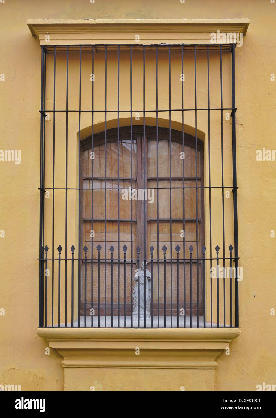 Immagine verticale di una parete arancione e di una finestra con bar con una statua della beata madre all'interno Foto Stock