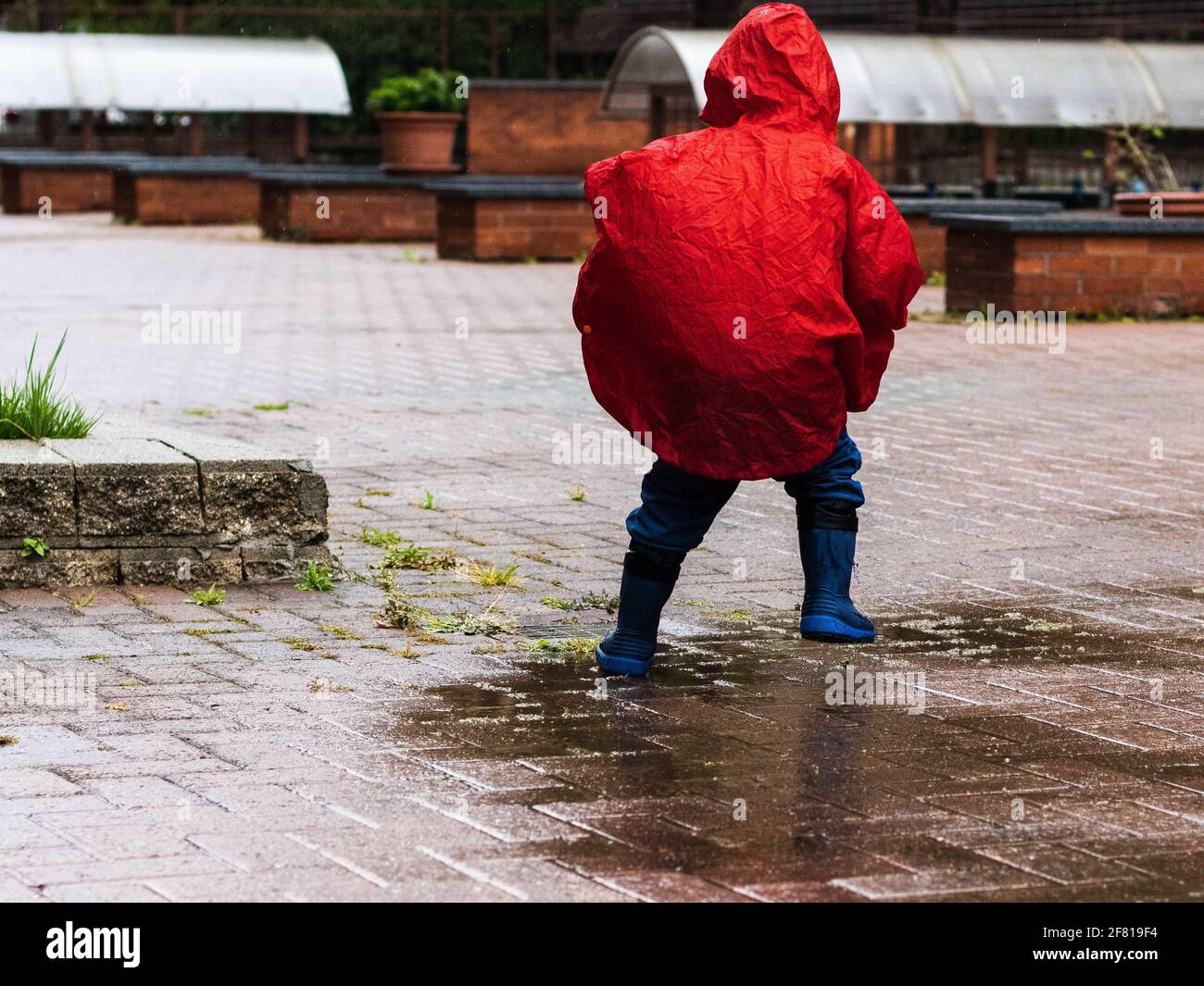 bambino piccolo irriconoscibile che gioca saltando in una pozza Foto Stock