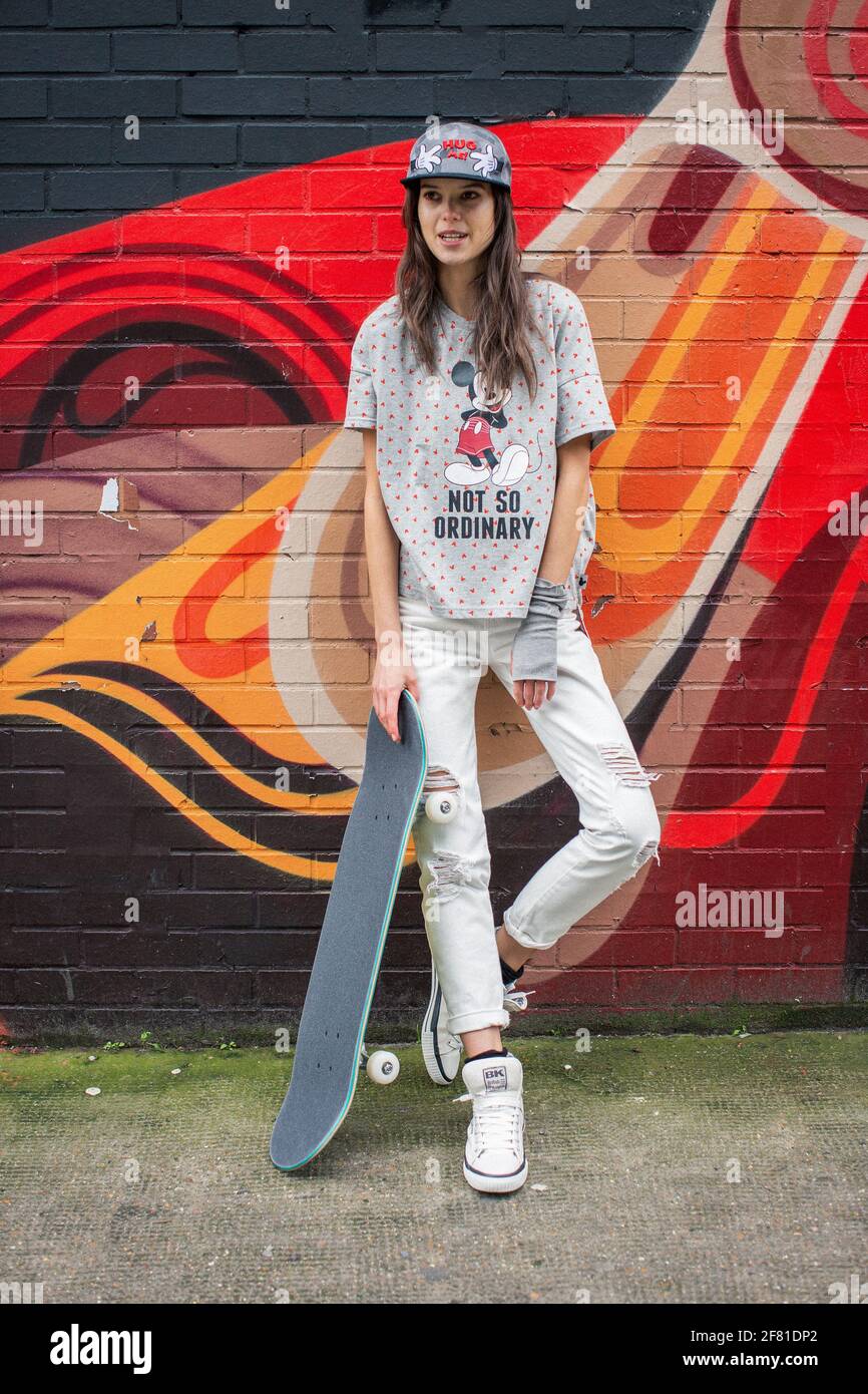 Adolescente ragazza con skateboard in piedi vicino a muro urbano con graffiti colorati a Shorditch a Londra , Regno Unito . Foto Stock