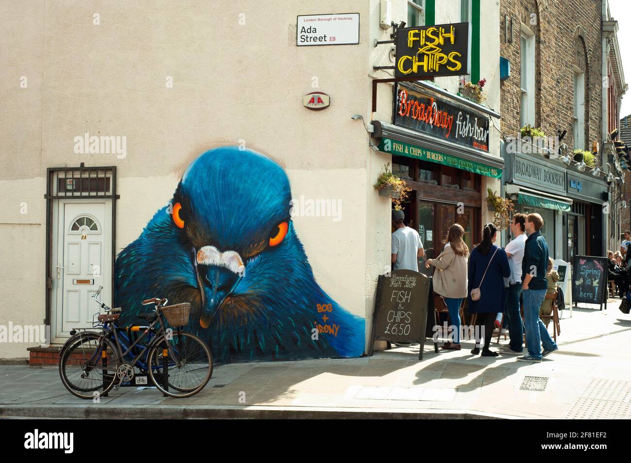 Le persone si allineano all'esterno di un negozio di fish & chips sul mercato di Broadway con un grande piccione (da boe e ironia) guardando dietro l'angolo. Londra, Regno Unito. Apr 2013 Foto Stock