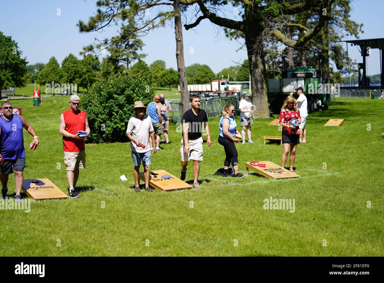 I maschi e le femmine giocano un gioco di lancio di sacco di fagioli all'evento del fine settimana di Walleye al parco del lago, come una comunità si riuniscono. Foto Stock I maschi e le femmine giocano un gioco di lancio di sacco di fagioli all'evento del fine settimana di Walleye al parco del lago, come una comunità si riuniscono. Foto Stock