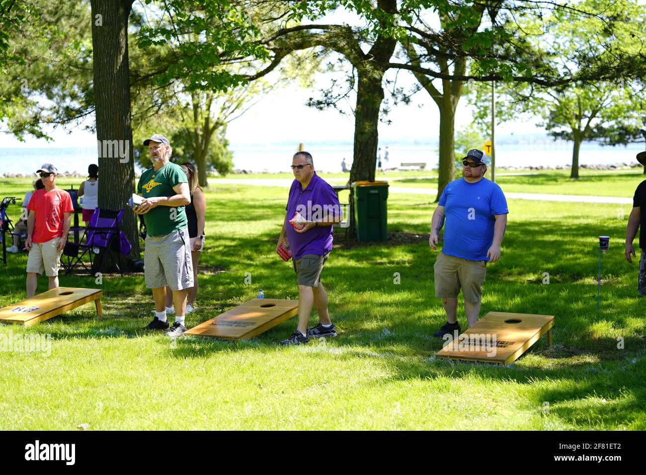 I maschi e le femmine giocano un gioco di lancio di sacco di fagioli all'evento del fine settimana di Walleye al parco del lago, come una comunità si riuniscono. Foto Stock I maschi e le femmine giocano un gioco di lancio di sacco di fagioli all'evento del fine settimana di Walleye al parco del lago, come una comunità si riuniscono. Foto Stock