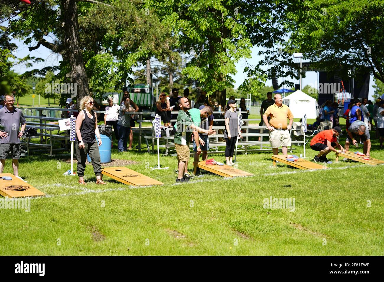 I maschi e le femmine giocano un gioco di lancio di sacco di fagioli all'evento del fine settimana di Walleye al parco del lago, come una comunità si riuniscono. Foto Stock I maschi e le femmine giocano un gioco di lancio di sacco di fagioli all'evento del fine settimana di Walleye al parco del lago, come una comunità si riuniscono. Foto Stock
