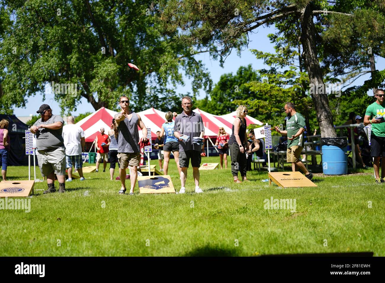 I maschi e le femmine giocano un gioco di lancio di sacco di fagioli all'evento del fine settimana di Walleye al parco del lago, come una comunità si riuniscono. Foto Stock I maschi e le femmine giocano un gioco di lancio di sacco di fagioli all'evento del fine settimana di Walleye al parco del lago, come una comunità si riuniscono. Foto Stock