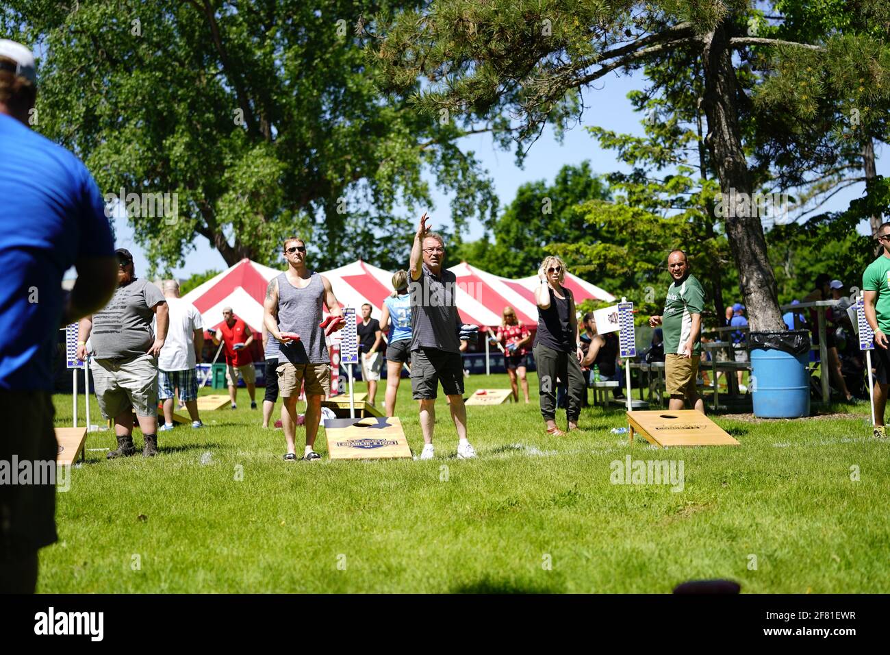 I maschi e le femmine giocano un gioco di lancio di sacco di fagioli all'evento del fine settimana di Walleye al parco del lago, come una comunità si riuniscono. Foto Stock I maschi e le femmine giocano un gioco di lancio di sacco di fagioli all'evento del fine settimana di Walleye al parco del lago, come una comunità si riuniscono. Foto Stock