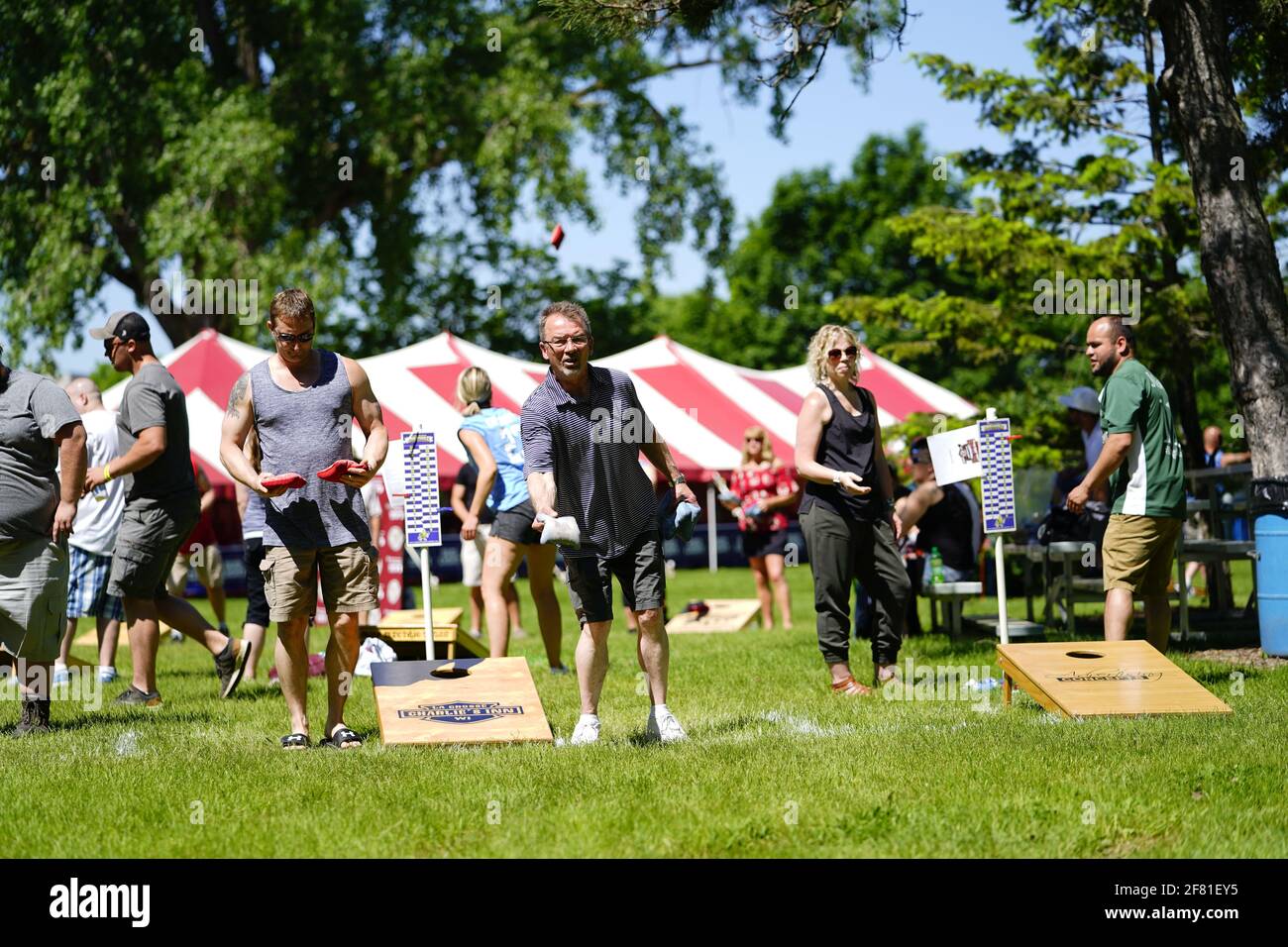 I maschi e le femmine giocano un gioco di lancio di sacco di fagioli all'evento del fine settimana di Walleye al parco del lago, come una comunità si riuniscono. Foto Stock I maschi e le femmine giocano un gioco di lancio di sacco di fagioli all'evento del fine settimana di Walleye al parco del lago, come una comunità si riuniscono. Foto Stock