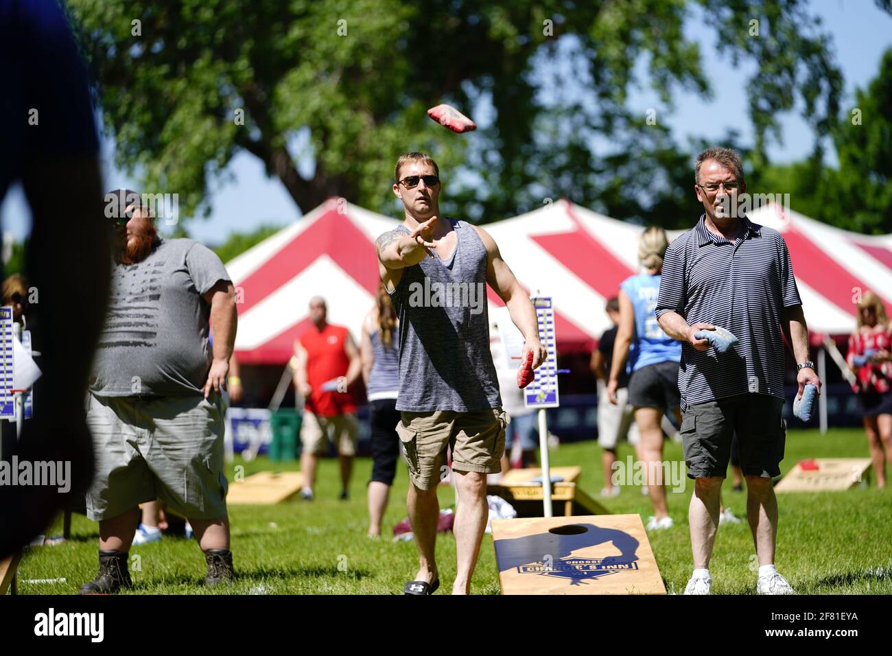 I maschi e le femmine giocano un gioco di lancio di sacco di fagioli all'evento del fine settimana di Walleye al parco del lago, come una comunità si riuniscono. Foto Stock I maschi e le femmine giocano un gioco di lancio di sacco di fagioli all'evento del fine settimana di Walleye al parco del lago, come una comunità si riuniscono. Foto Stock