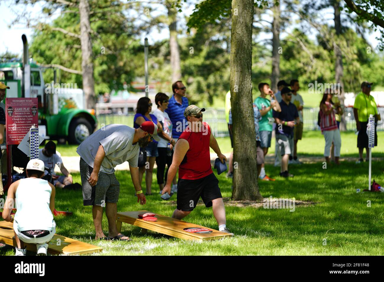 I maschi e le femmine giocano un gioco di lancio di sacco di fagioli all'evento del fine settimana di Walleye al parco del lago, come una comunità si riuniscono. Foto Stock I maschi e le femmine giocano un gioco di lancio di sacco di fagioli all'evento del fine settimana di Walleye al parco del lago, come una comunità si riuniscono. Foto Stock