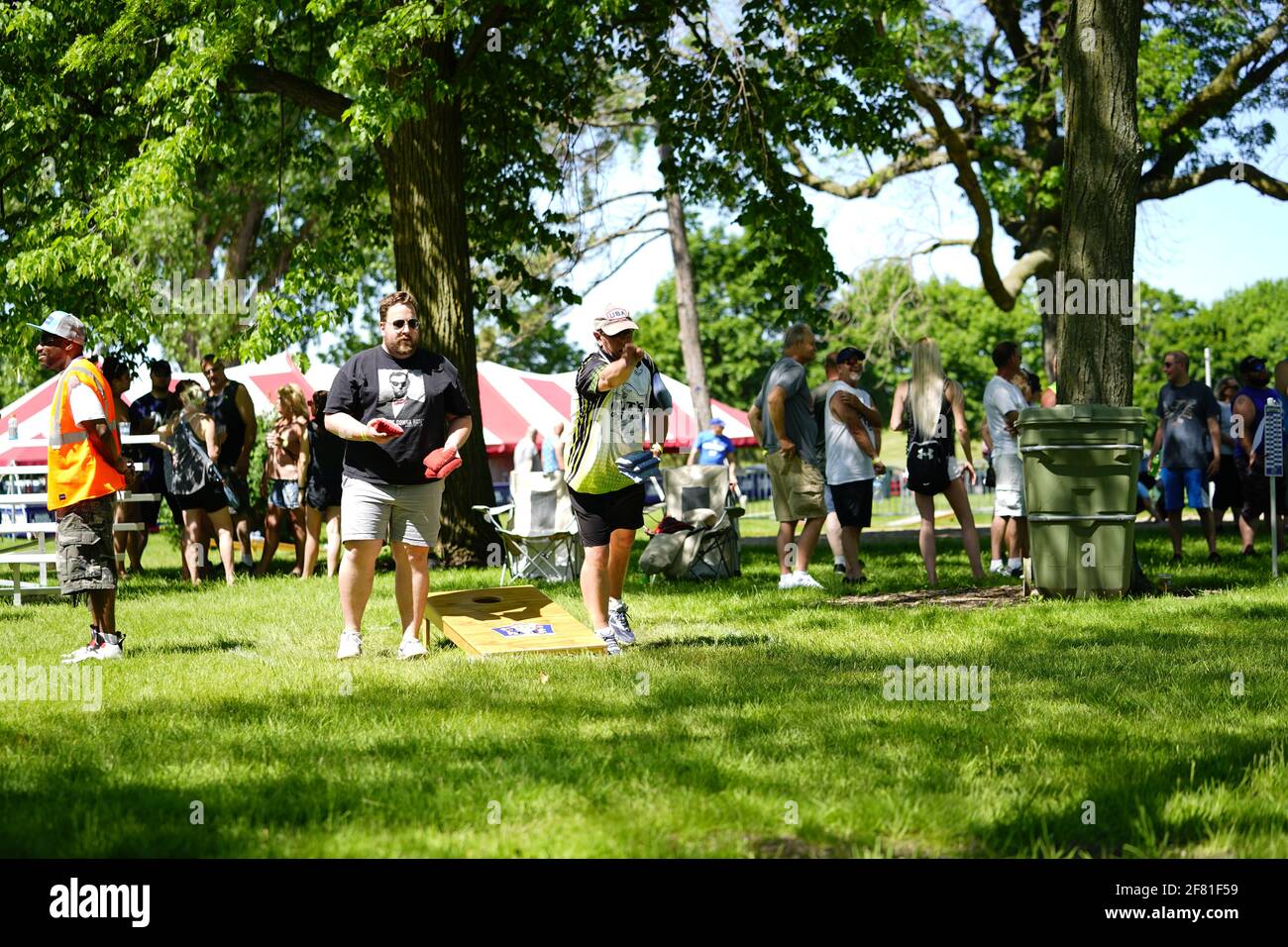 I maschi e le femmine giocano un gioco di lancio di sacco di fagioli all'evento del fine settimana di Walleye al parco del lago, come una comunità si riuniscono. Foto Stock I maschi e le femmine giocano un gioco di lancio di sacco di fagioli all'evento del fine settimana di Walleye al parco del lago, come una comunità si riuniscono. Foto Stock