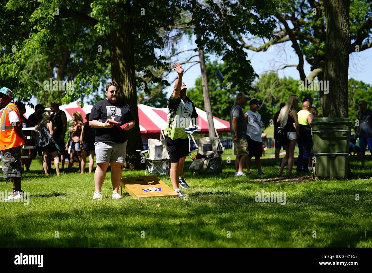 I maschi e le femmine giocano un gioco di lancio di sacco di fagioli all'evento del fine settimana di Walleye al parco del lago, come una comunità si riuniscono. Foto Stock I maschi e le femmine giocano un gioco di lancio di sacco di fagioli all'evento del fine settimana di Walleye al parco del lago, come una comunità si riuniscono. Foto Stock