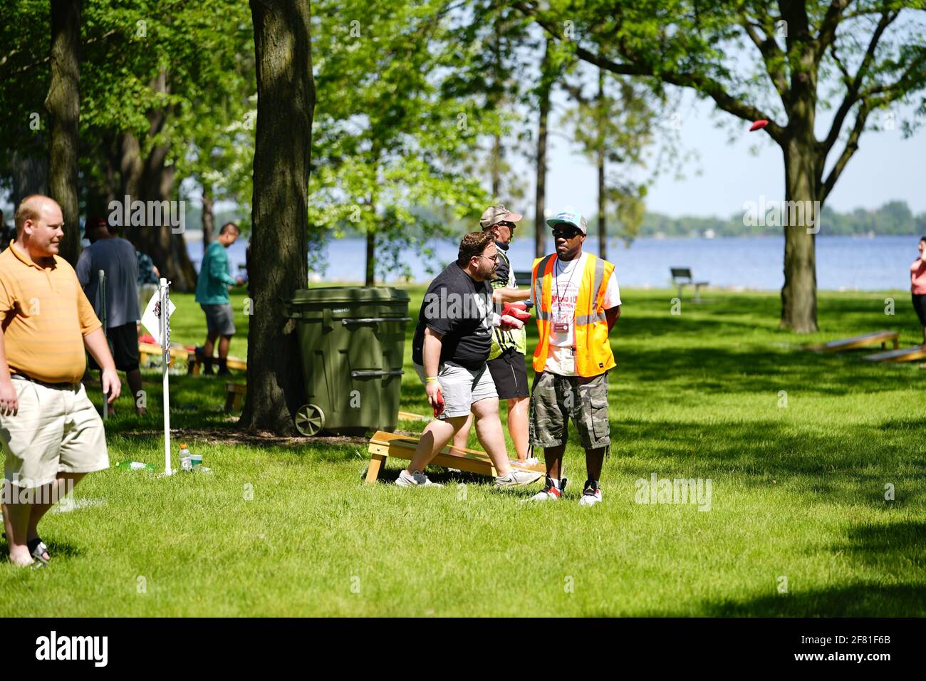 I maschi e le femmine giocano un gioco di lancio di sacco di fagioli all'evento del fine settimana di Walleye al parco del lago, come una comunità si riuniscono. Foto Stock I maschi e le femmine giocano un gioco di lancio di sacco di fagioli all'evento del fine settimana di Walleye al parco del lago, come una comunità si riuniscono. Foto Stock