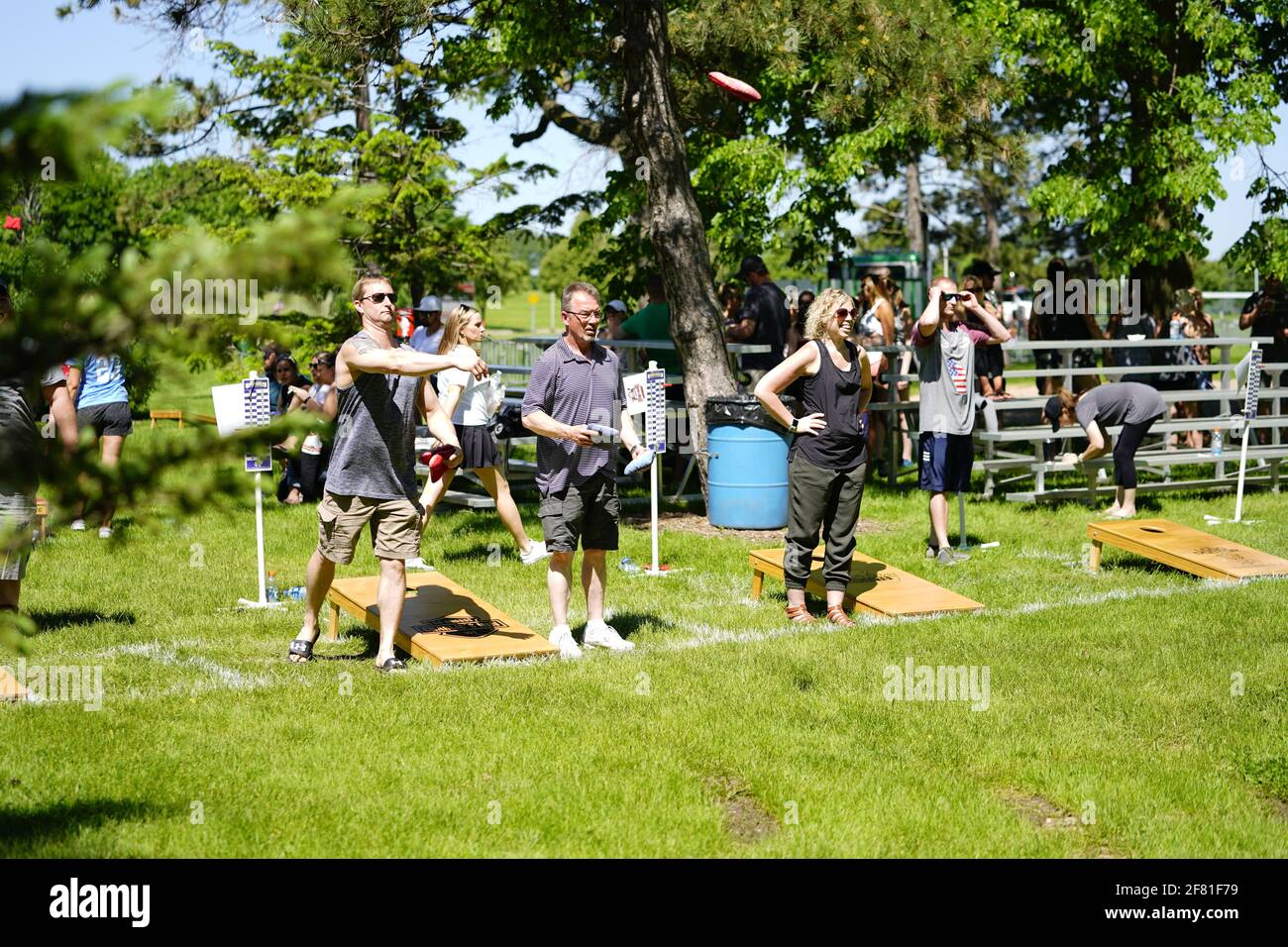 I maschi e le femmine giocano un gioco di lancio di sacco di fagioli all'evento del fine settimana di Walleye al parco del lago, come una comunità si riuniscono. Foto Stock I maschi e le femmine giocano un gioco di lancio di sacco di fagioli all'evento del fine settimana di Walleye al parco del lago, come una comunità si riuniscono. Foto Stock