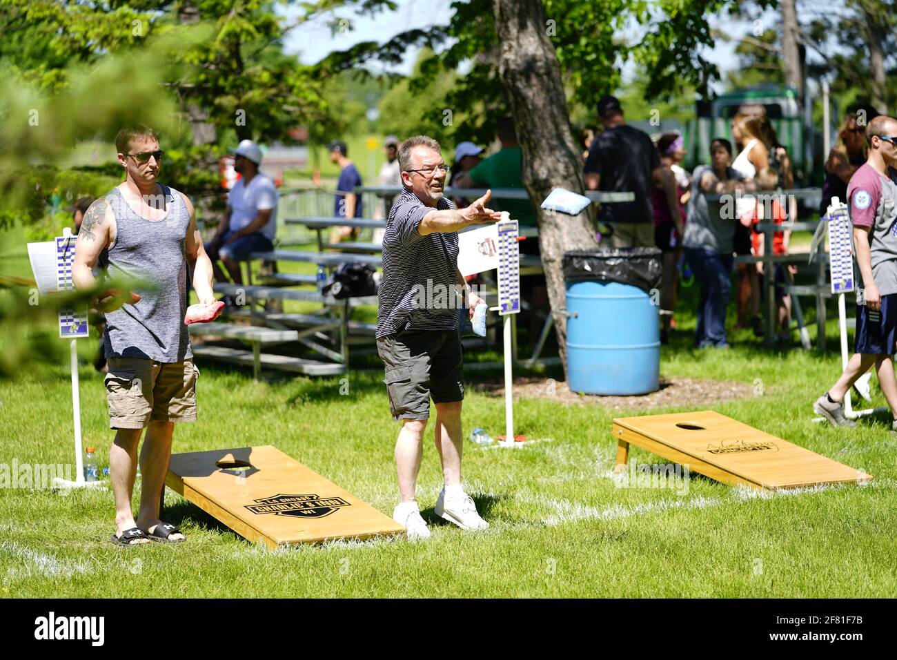 I maschi e le femmine giocano un gioco di lancio di sacco di fagioli all'evento del fine settimana di Walleye al parco del lago, come una comunità si riuniscono. Foto Stock I maschi e le femmine giocano un gioco di lancio di sacco di fagioli all'evento del fine settimana di Walleye al parco del lago, come una comunità si riuniscono. Foto Stock