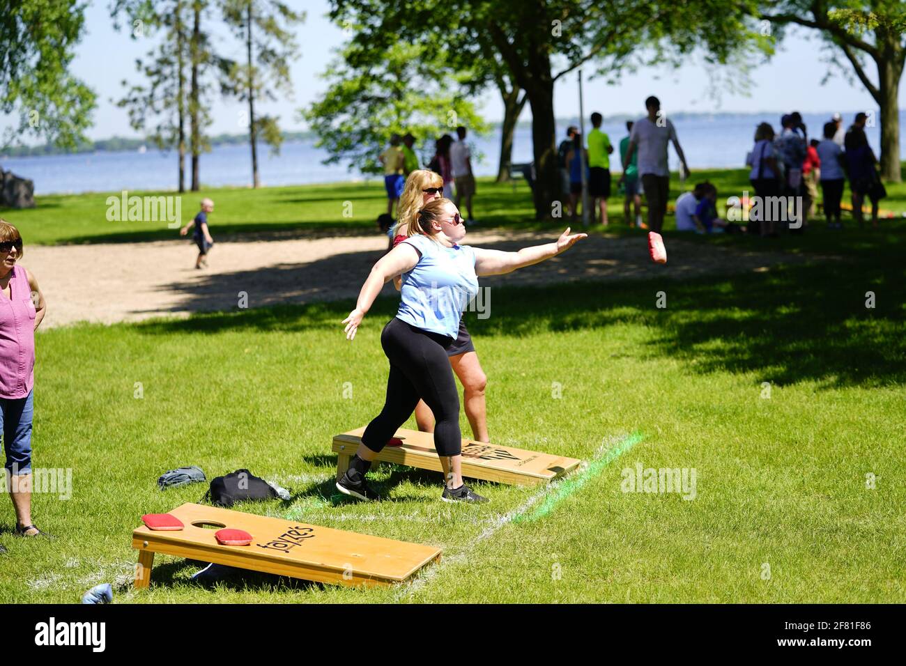 I maschi e le femmine giocano un gioco di lancio di sacco di fagioli all'evento del fine settimana di Walleye al parco del lago, come una comunità si riuniscono. Foto Stock I maschi e le femmine giocano un gioco di lancio di sacco di fagioli all'evento del fine settimana di Walleye al parco del lago, come una comunità si riuniscono. Foto Stock