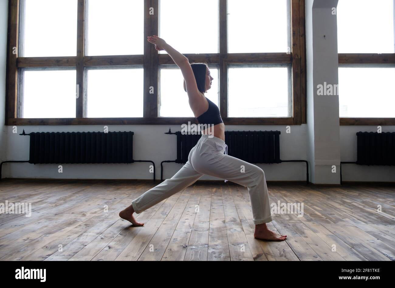 Donna nel suo soggiorno in posizione guerriero yoga. Foto Stock