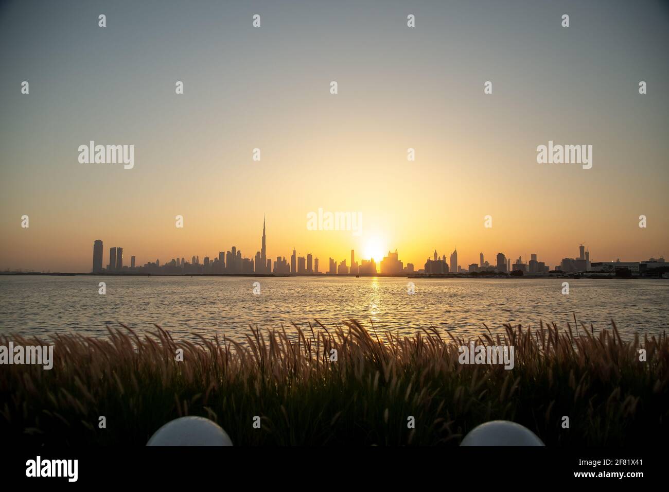 Il paesaggio urbano di Dubai al tramonto con Burj Khalifa preso dal porto con acqua e erba di fronte Foto Stock