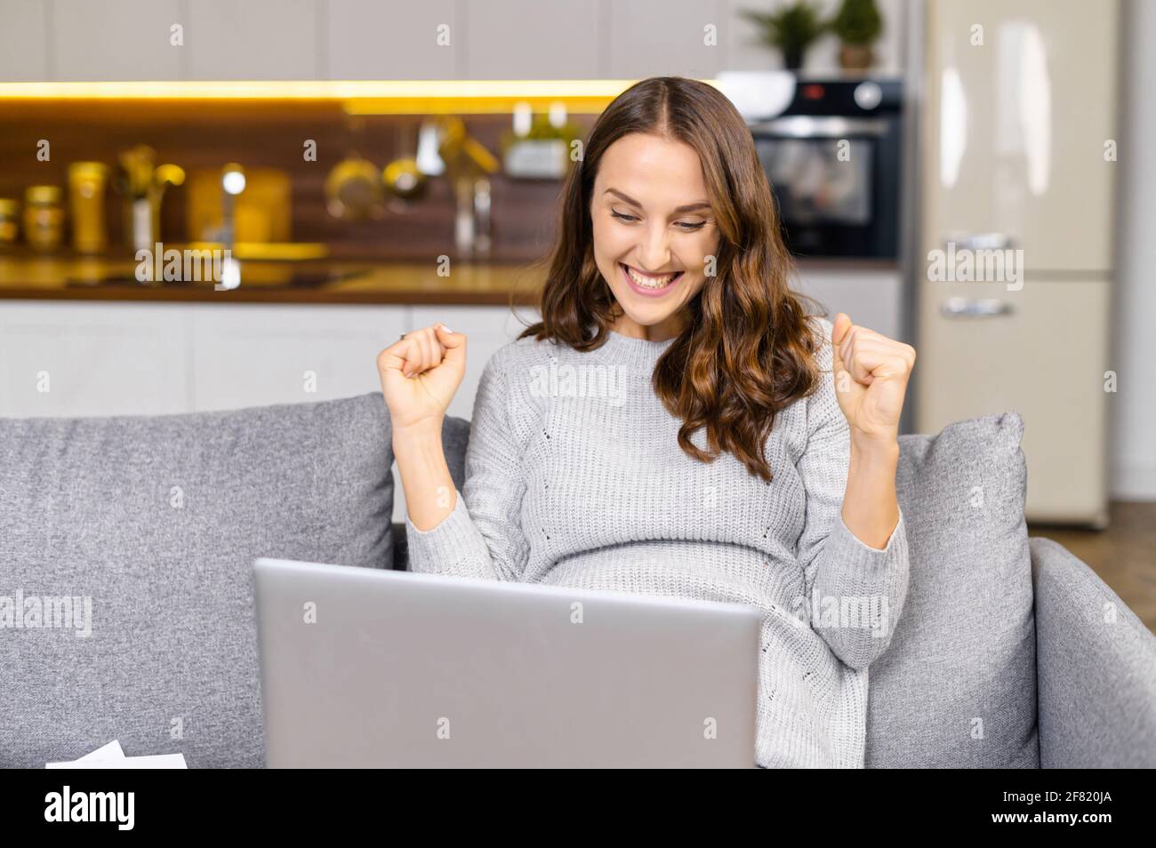 La donna esultata si rallegra finalmente finito il lavoro, seduto sul divano a casa, guarda lo schermo del portatile e gesturando sì, donna entusiasta felice con successo risultato, braccia estatiche sollevate Foto Stock