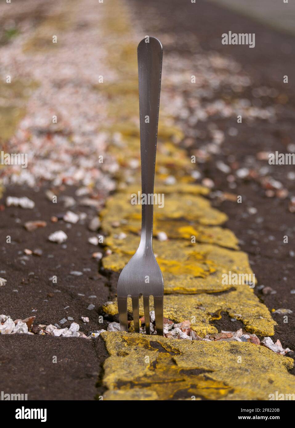 Un bivio sulla strada. Una forcella in acciaio inox che si infila in una strada, per indicare scelta, dilemma, opzioni e alternative attraverso il mezzo della metafora. Foto Stock