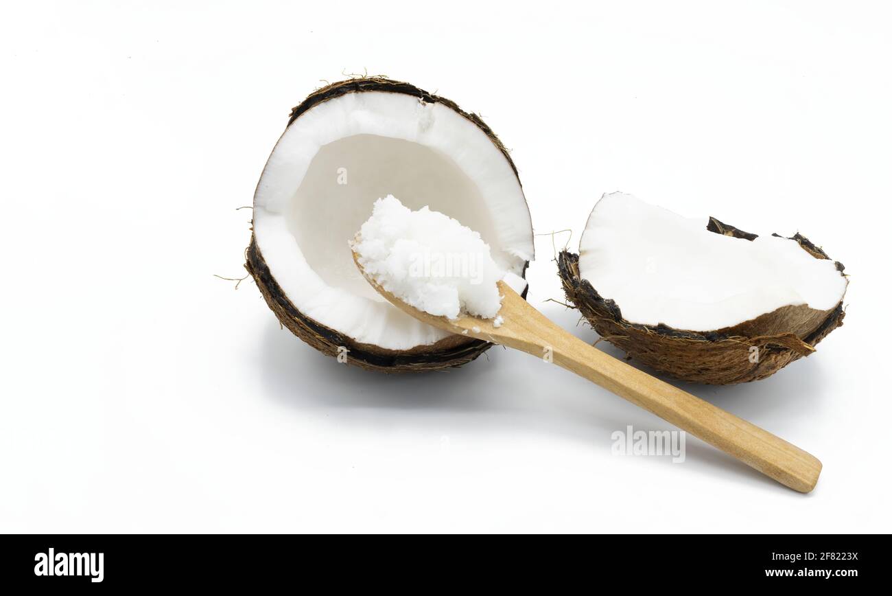 Concetto di cibo sano, un cucchiaio di legno con olio di cocco allo stato solido accanto a un cocco dimezzato su sfondo bianco Foto Stock