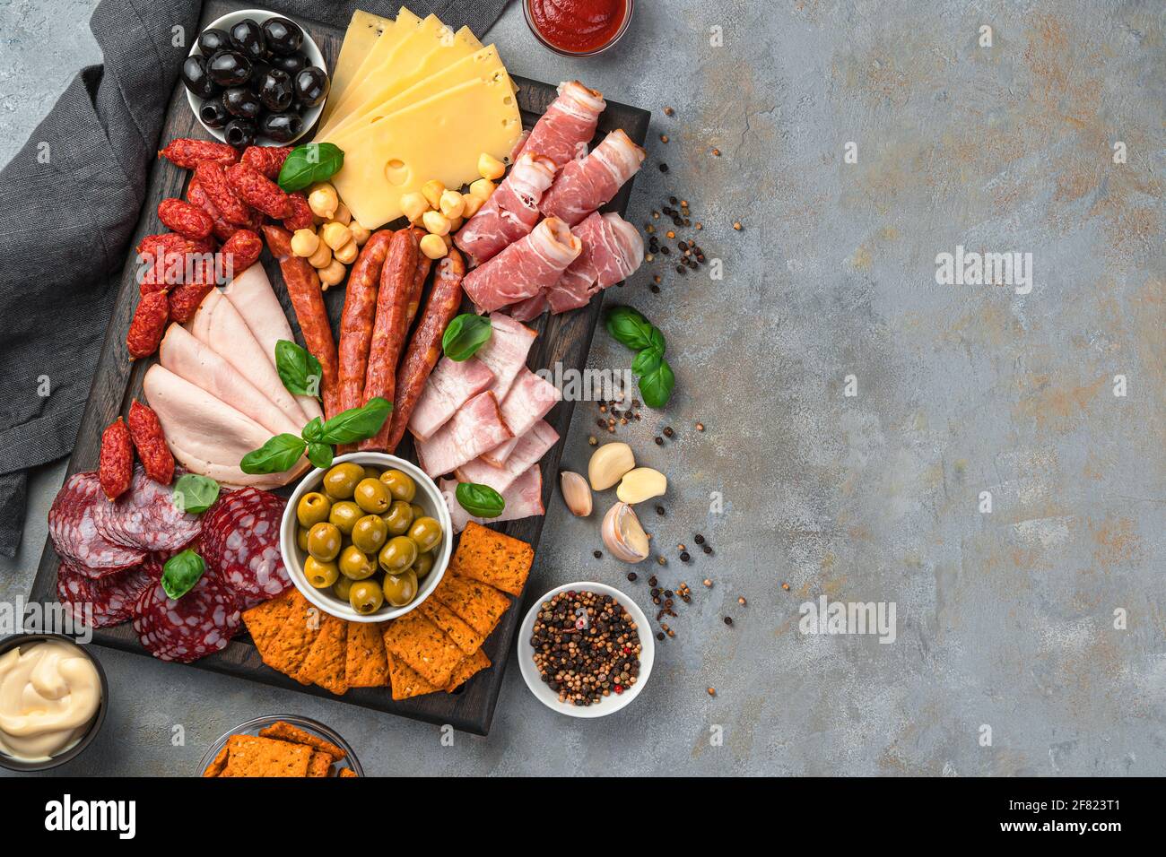 Salumi da caccia, salumi, pancetta, prosciutto, vari tipi di formaggio, olive e spezie su un tagliere su sfondo grigio. Affettati di carne, antipasto. Foto Stock