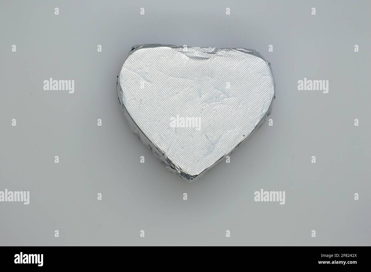 Wrapper di caramelle al cioccolato di colore argento. Forma del cuore su sfondo grigio. Foto Stock