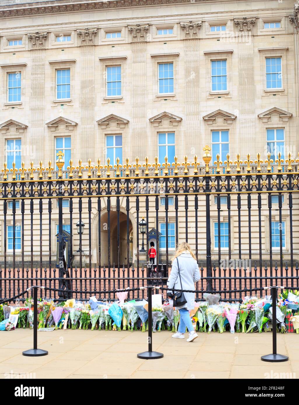 Buckingham Palace, Londra. Un membro del pubblico che pone un tributo floreale al Principe Filippo con la Guardia del Queens in piedi Sentry, Londra, Regno Unito, 2 aprile Foto Stock