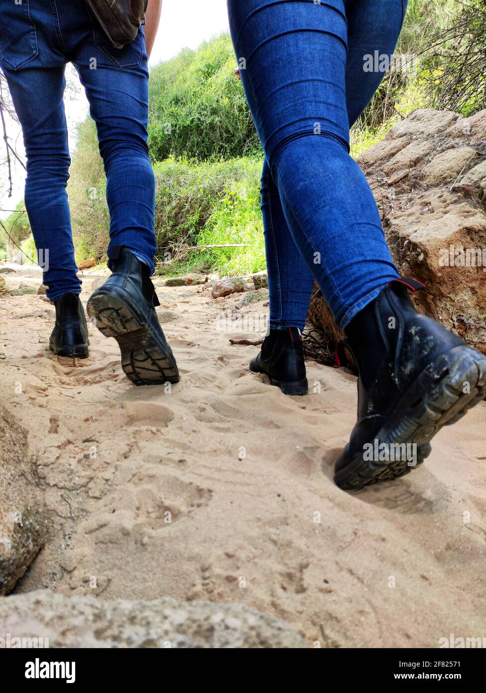 Un primo piano di gambe di una coppia in jeans a piedi sul sentiero  sabbioso indossare scarpe da trekking Foto stock - Alamy