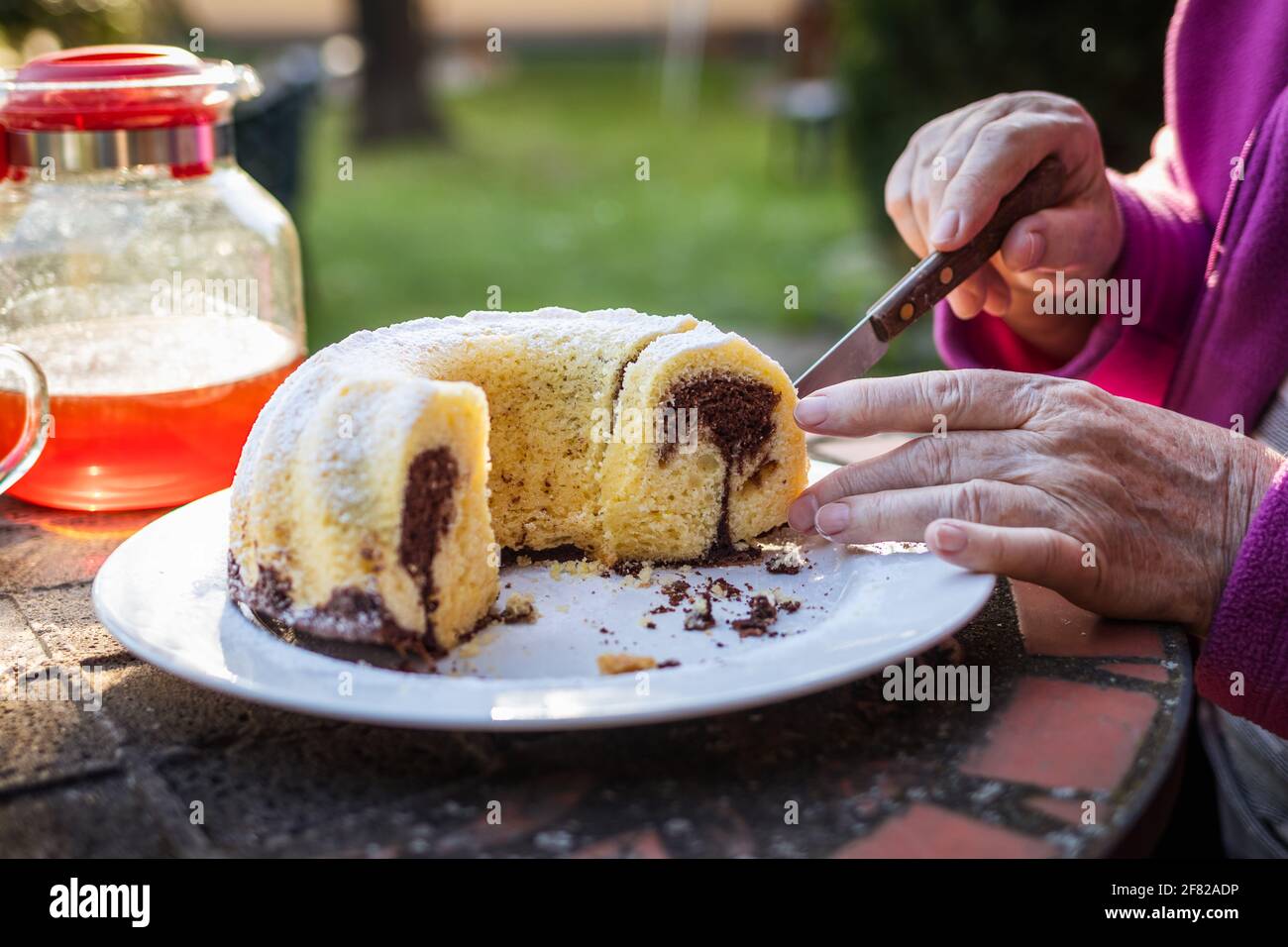 Donna anziana che serve fetta di torta all'aperto. Torta in ciambelle di marmo sul tavolo da picnic Foto Stock