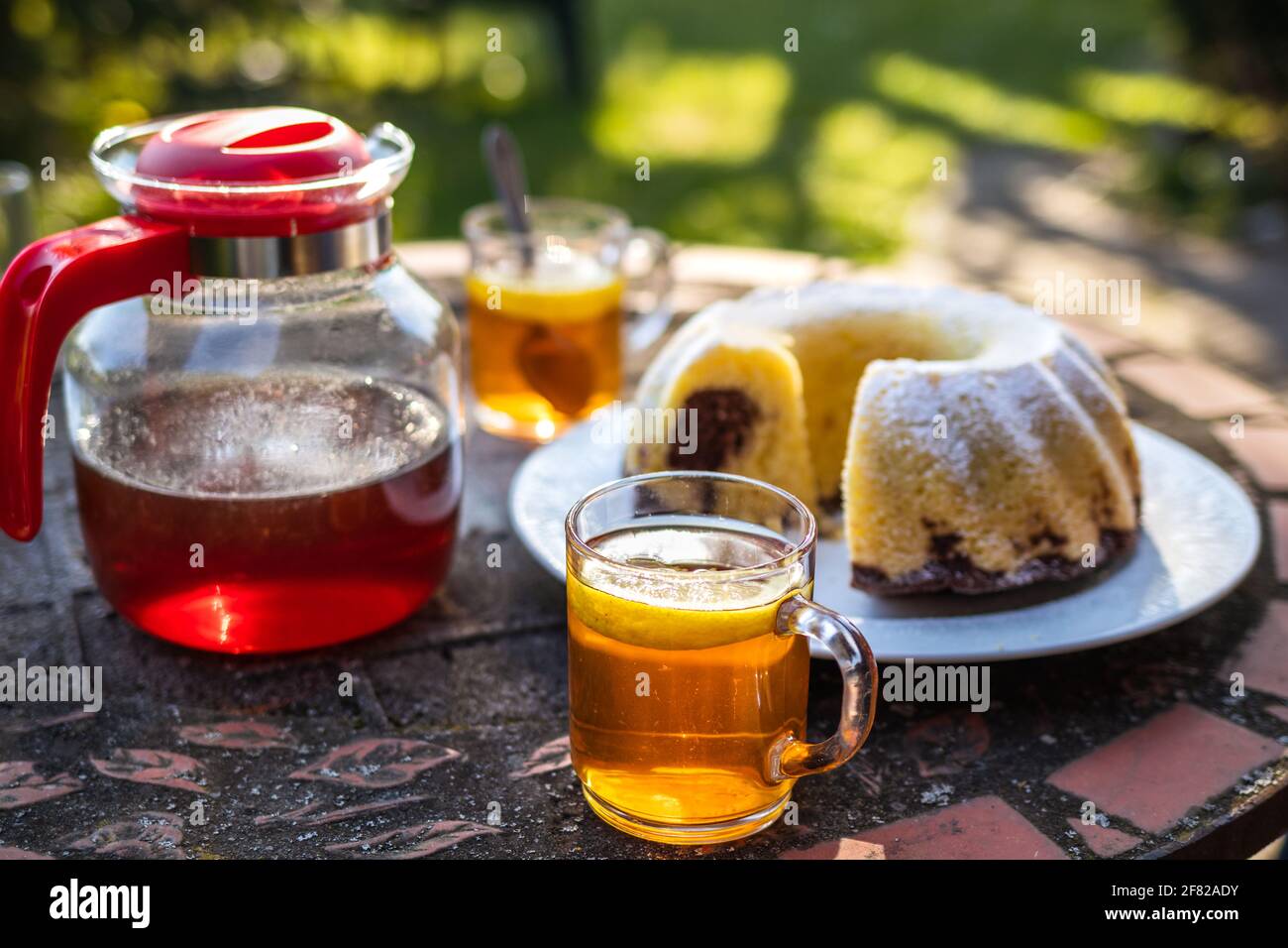 Tè in tazza e teiera con torta in padella sul tavolo all'aperto. Serve dessert e bevande calde nel giardino di primavera. Picnic in primavera Foto Stock