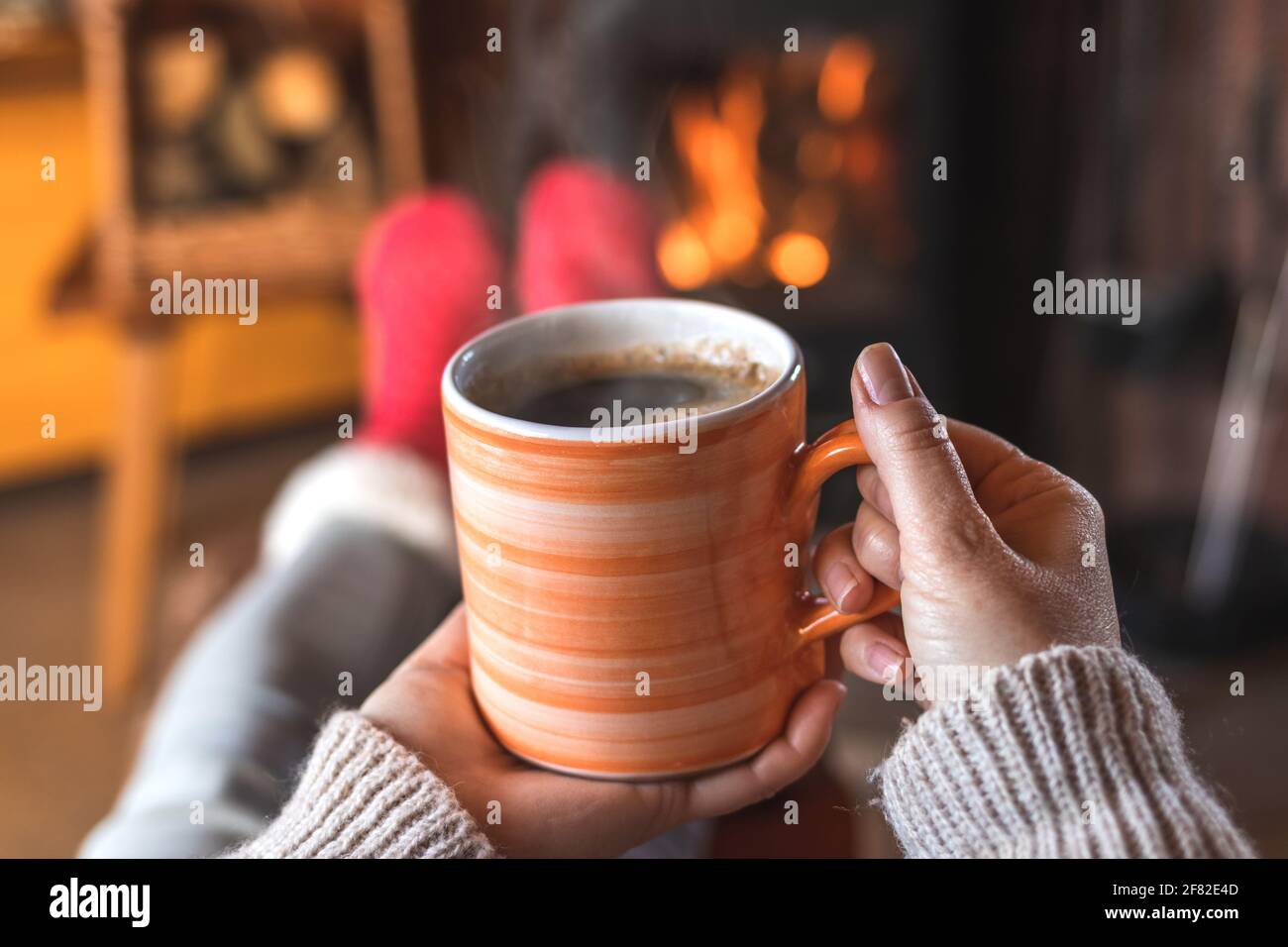 Donna che tiene in mano una tazza di caffè e si rilassa davanti al caminetto. Punto di vista. Donna rilassante e bere caffè caldo al chiuso Foto Stock
