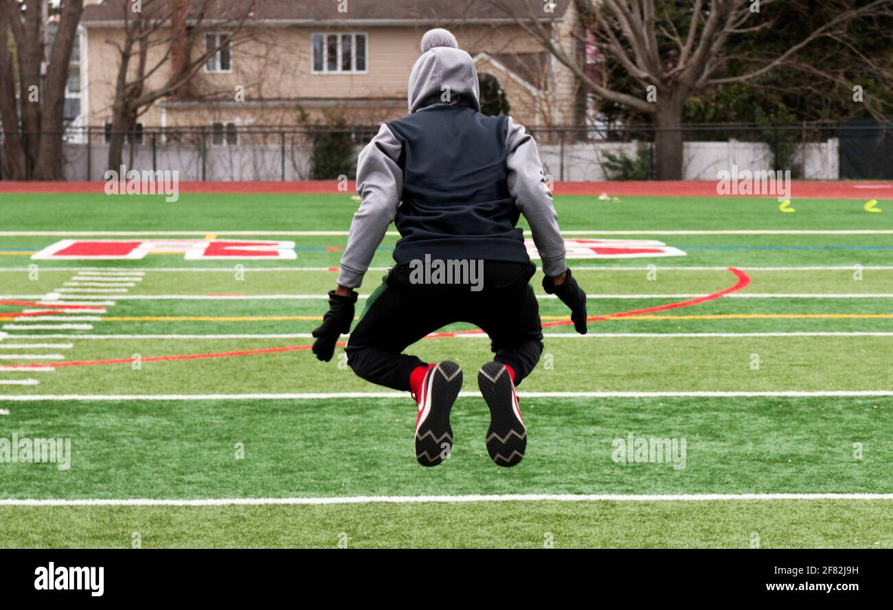 Vista posteriore di un atleta maschile adolescente che salta in aria forza e agilità pratica in pista e sul campo. Foto Stock