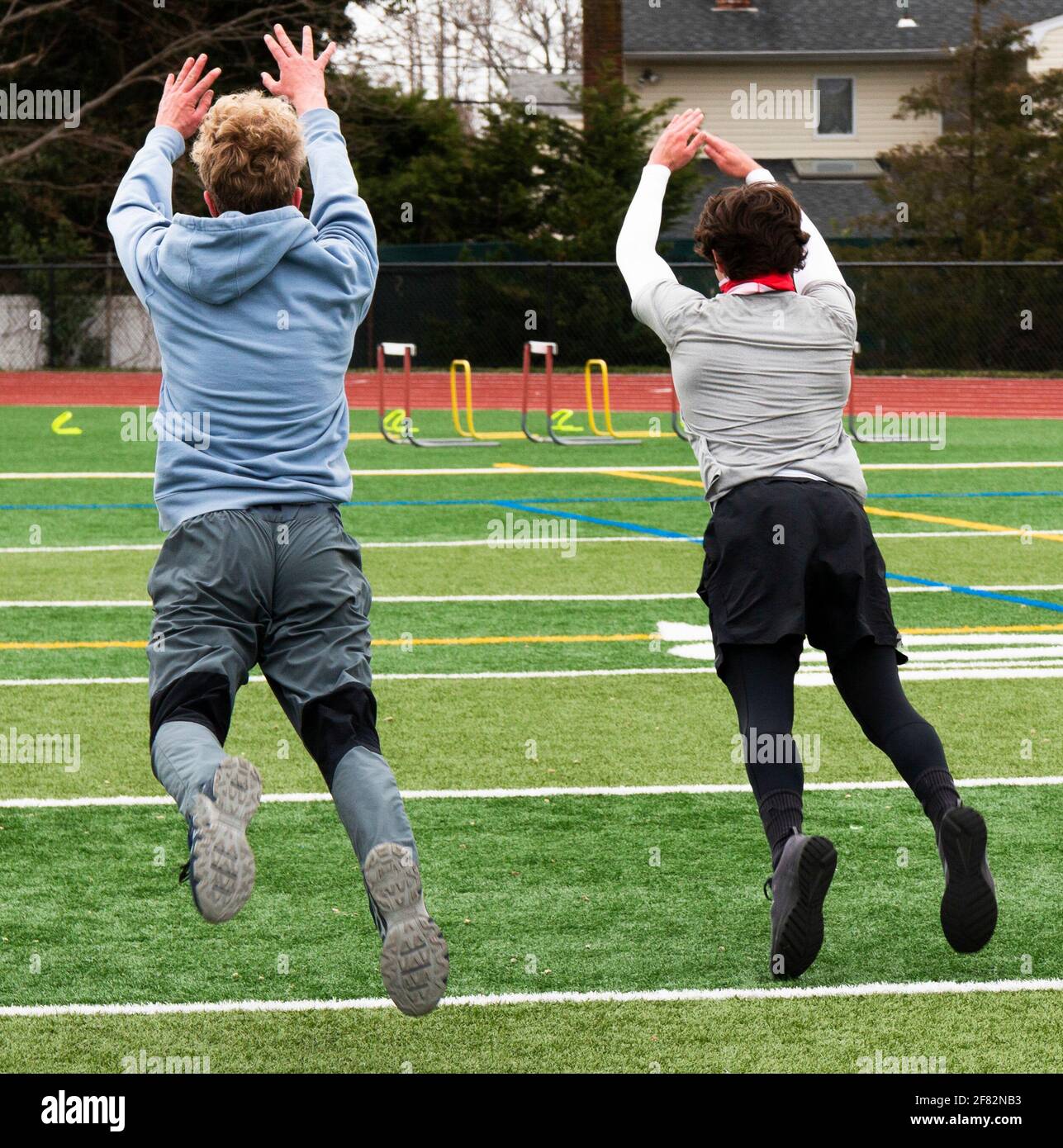 Due ragazzi a metà volo mentre saltano in pista e campo forza e agilità pratica su un campo erboso verde. Foto Stock