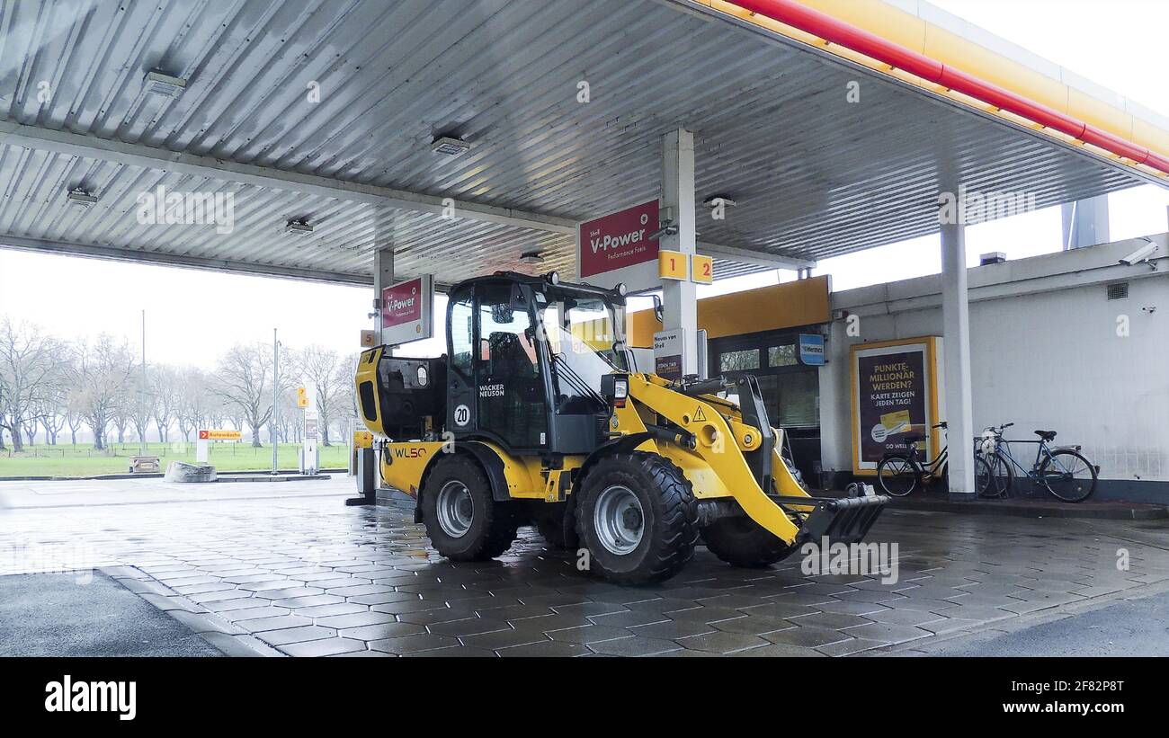 Lünen DORTMUND, GERMANIA - 07 aprile 2021: Escavatore giallo per veicoli da costruzione in Germania rifornimenti di benzina presso un distributore di benzina. La foto appare come un bi Foto Stock