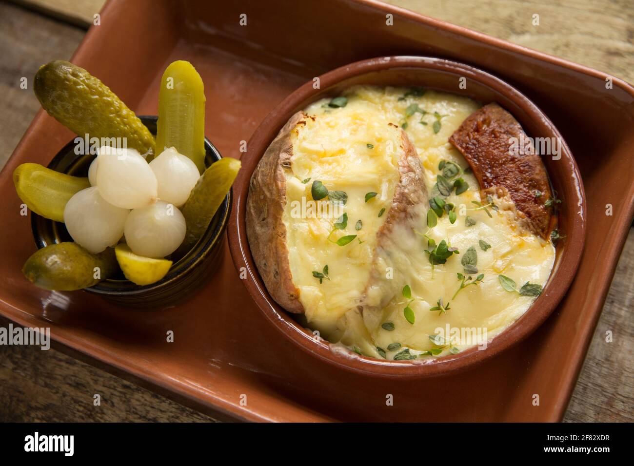 Un piatto fatto in casa di Raclette fuso, una patata al forno e salsiccia di chorizo alla griglia servita con cetriolini e cipolle sottaceto. Raclette ha avuto origine in Foto Stock