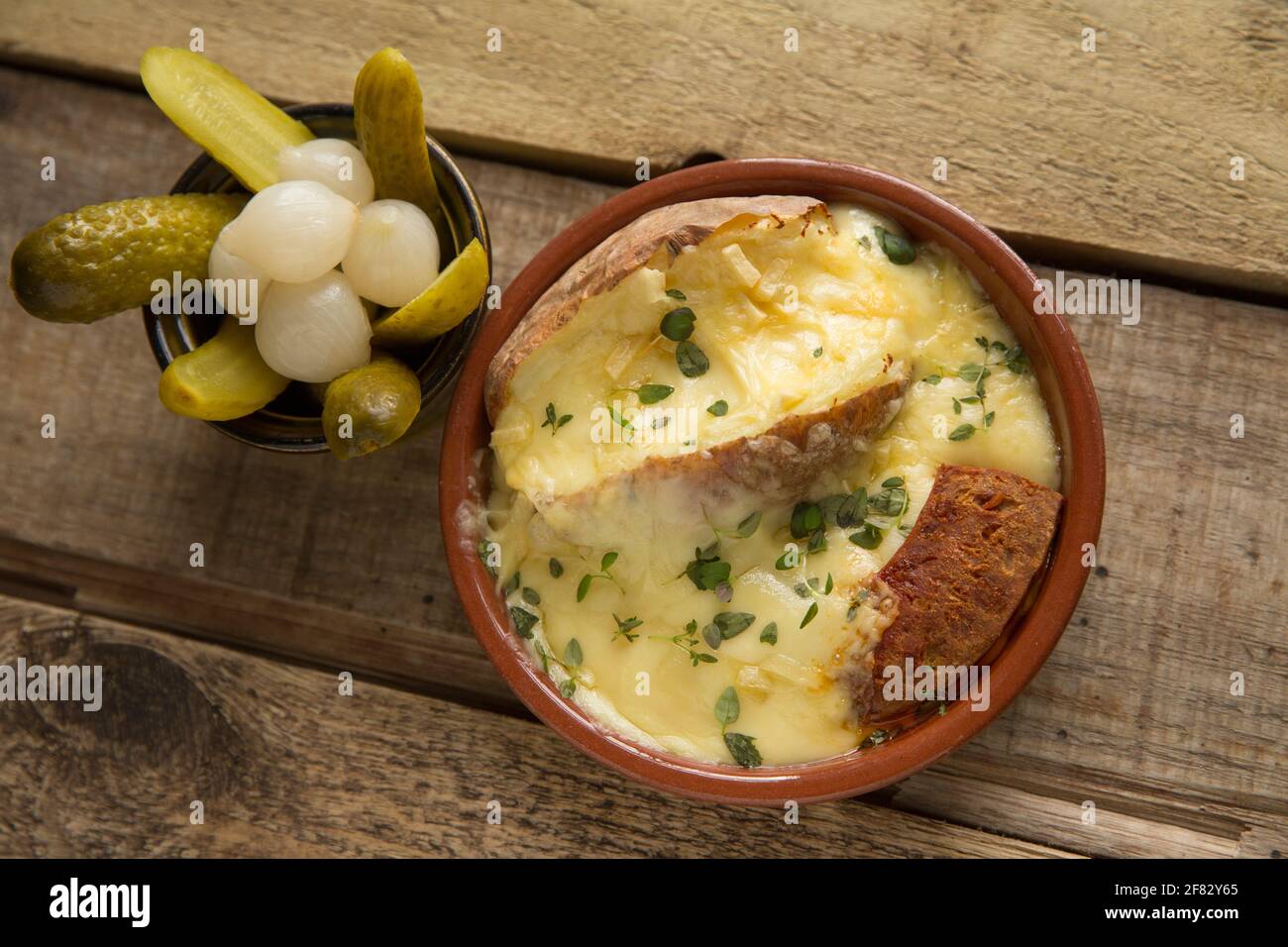 Un piatto fatto in casa di Raclette fuso, una patata al forno e salsiccia di chorizo alla griglia servita con cetriolini e cipolle sottaceto. Raclette ha avuto origine in Foto Stock