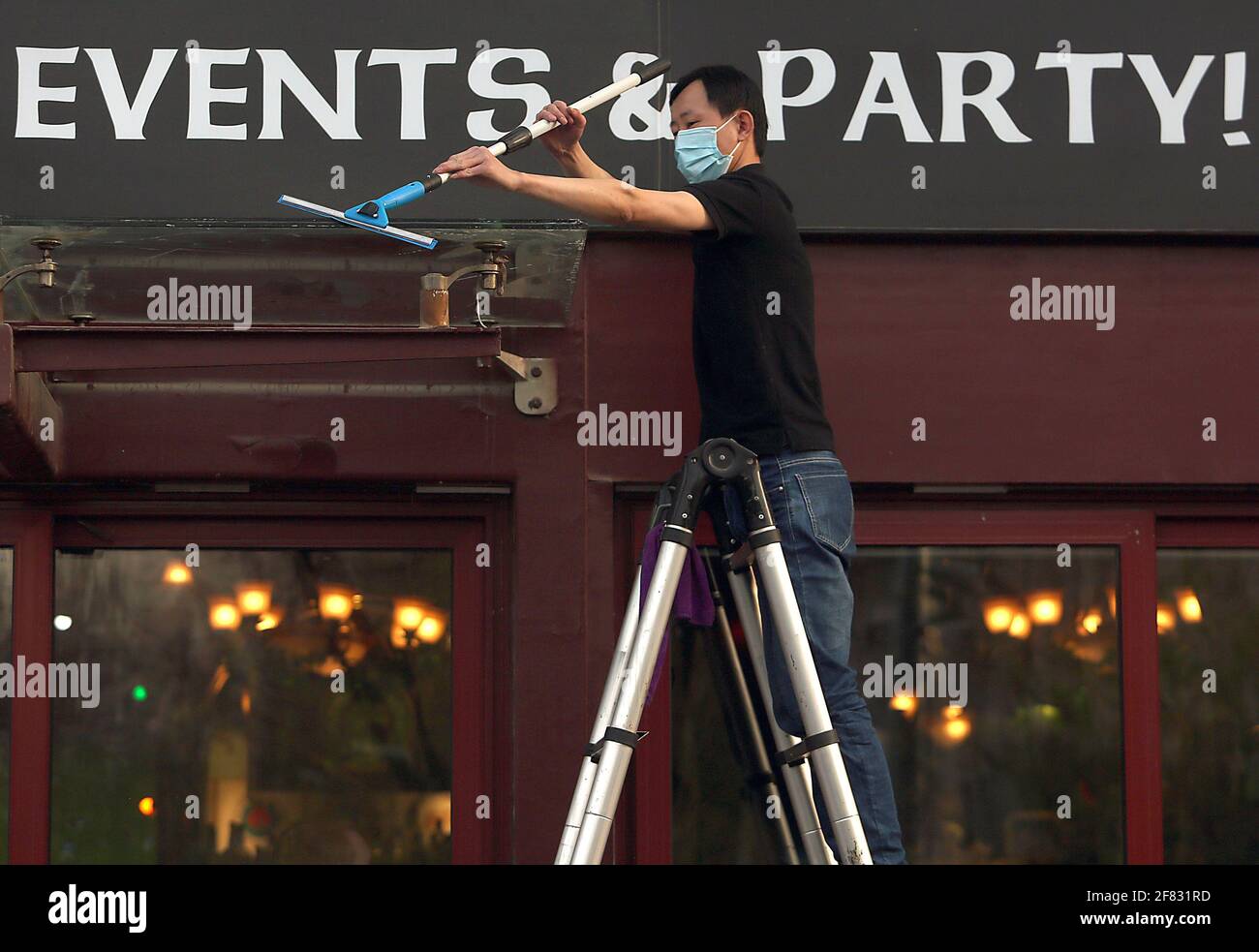 Pechino, Cina. 11 Apr 2021. Un membro dello staff cinese indossa una maschera protettiva mentre pulisce l'esterno di un popolare bar occidentale, completamente aperto per affari, a Pechino domenica 11 aprile 2021. La capitale cinese ha ridotto l'uso obbligatorio di maschere protettive, tranne che sui trasporti pubblici, e l'allontanamento sociale, mentre la città torna lentamente alla vita pre-covid 19 con ristoranti, aziende e scuole completamente aperti. Foto di Stephen Shaver/UPI Credit: UPI/Alamy Live News Foto Stock