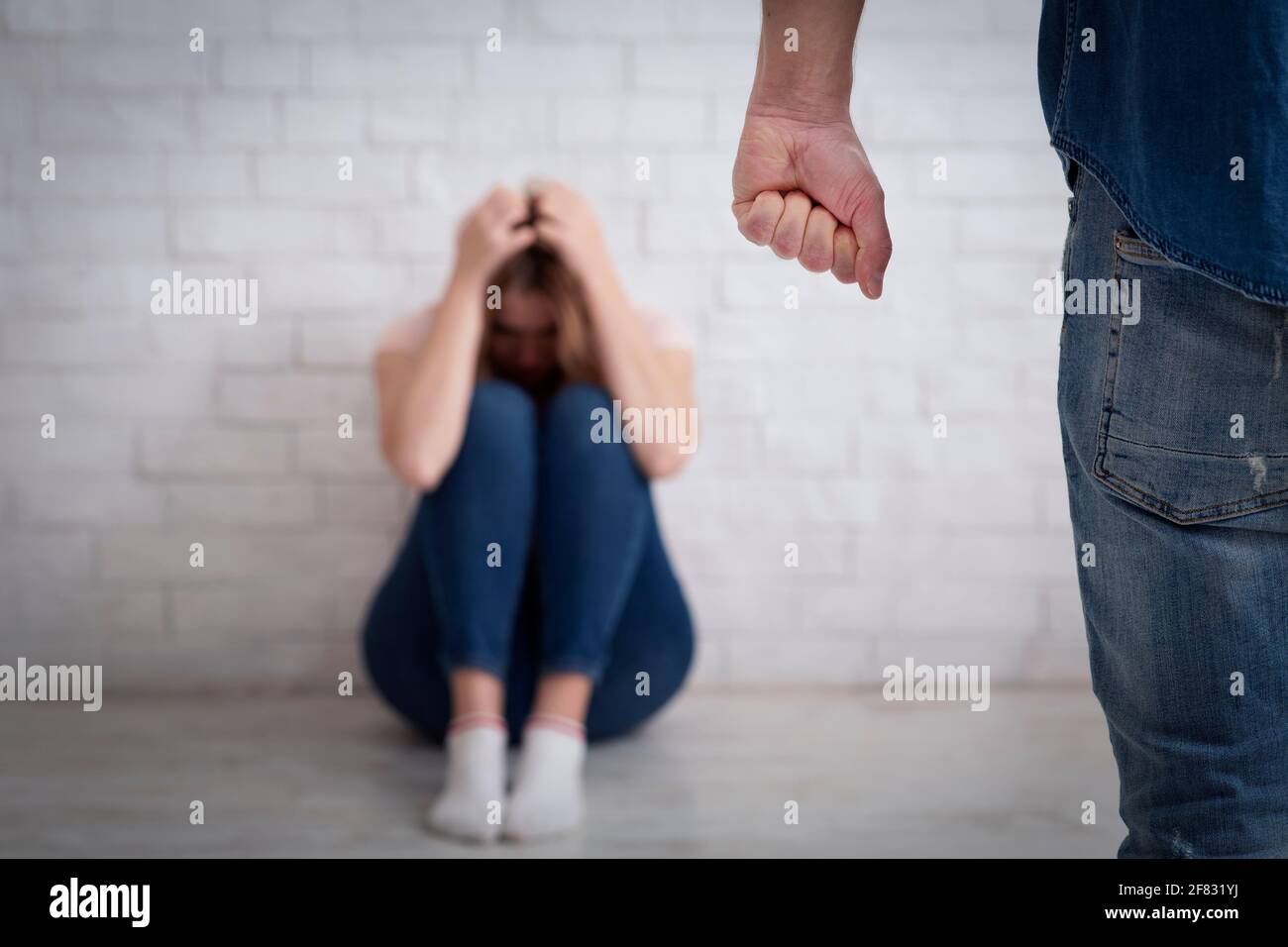 Violenza domestica, tirannia e battitura. La donna terrorizzata ricopre la testa con le mani e si siede sul pavimento Foto Stock