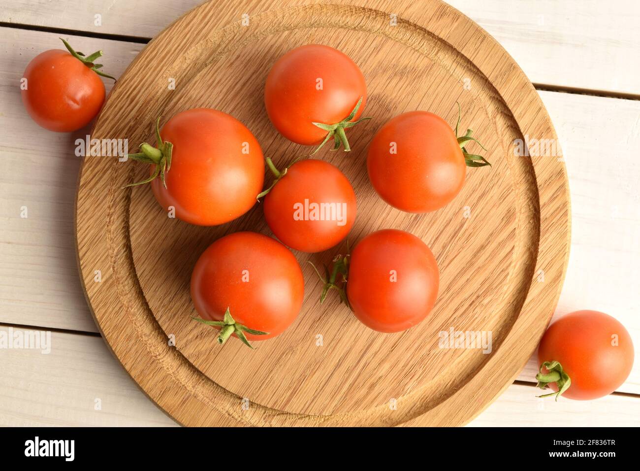 Diversi pomodori rossi e organici succosi su un vassoio di legno rotondo, primo piano, su un tavolo di legno bianco. Foto Stock