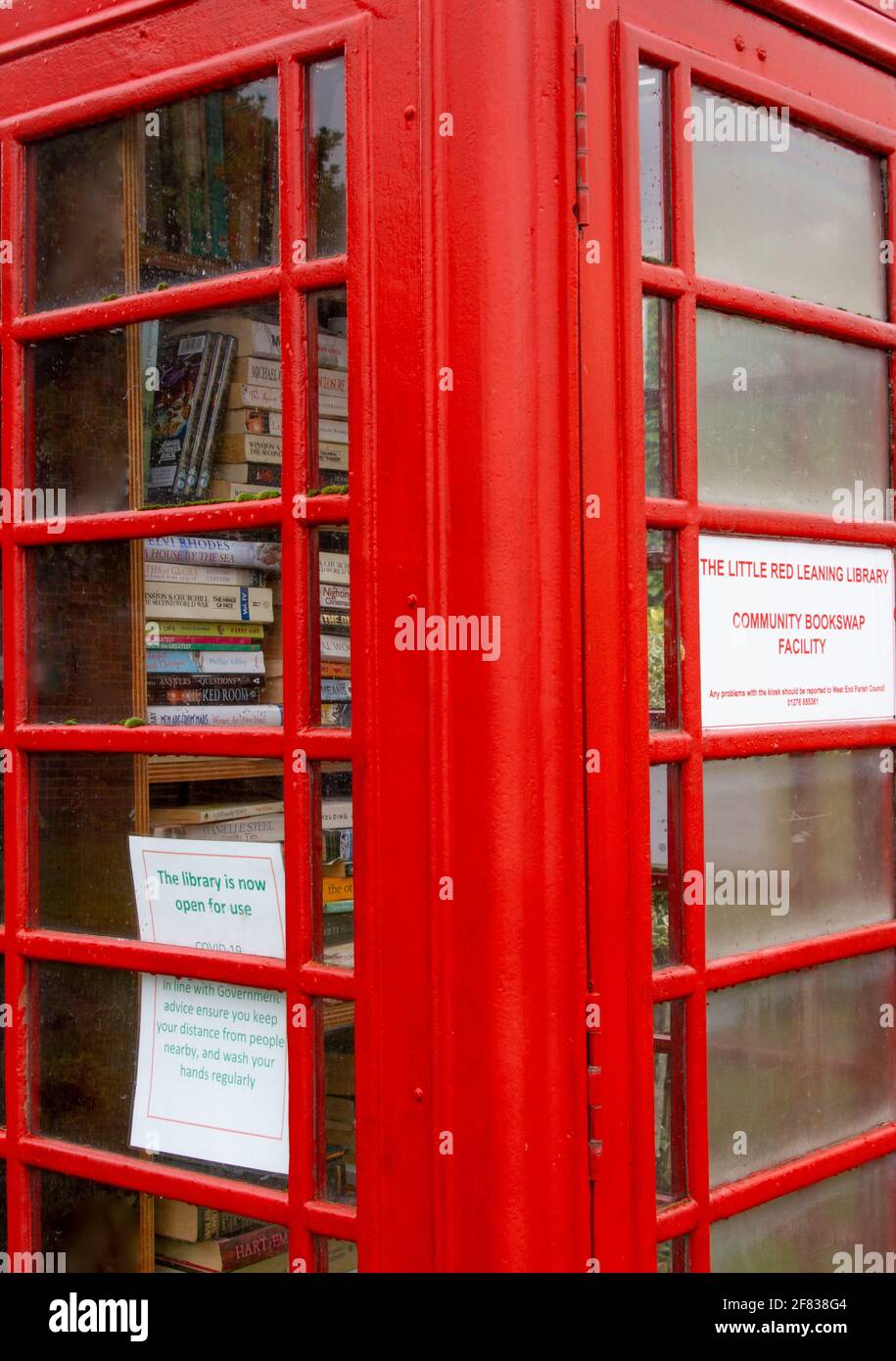 Primo piano di una tradizionale scatola telefonica rossa ora in uso come scambio di libri della comunità locale nel villaggio di West End, Woking, Surrey Foto Stock