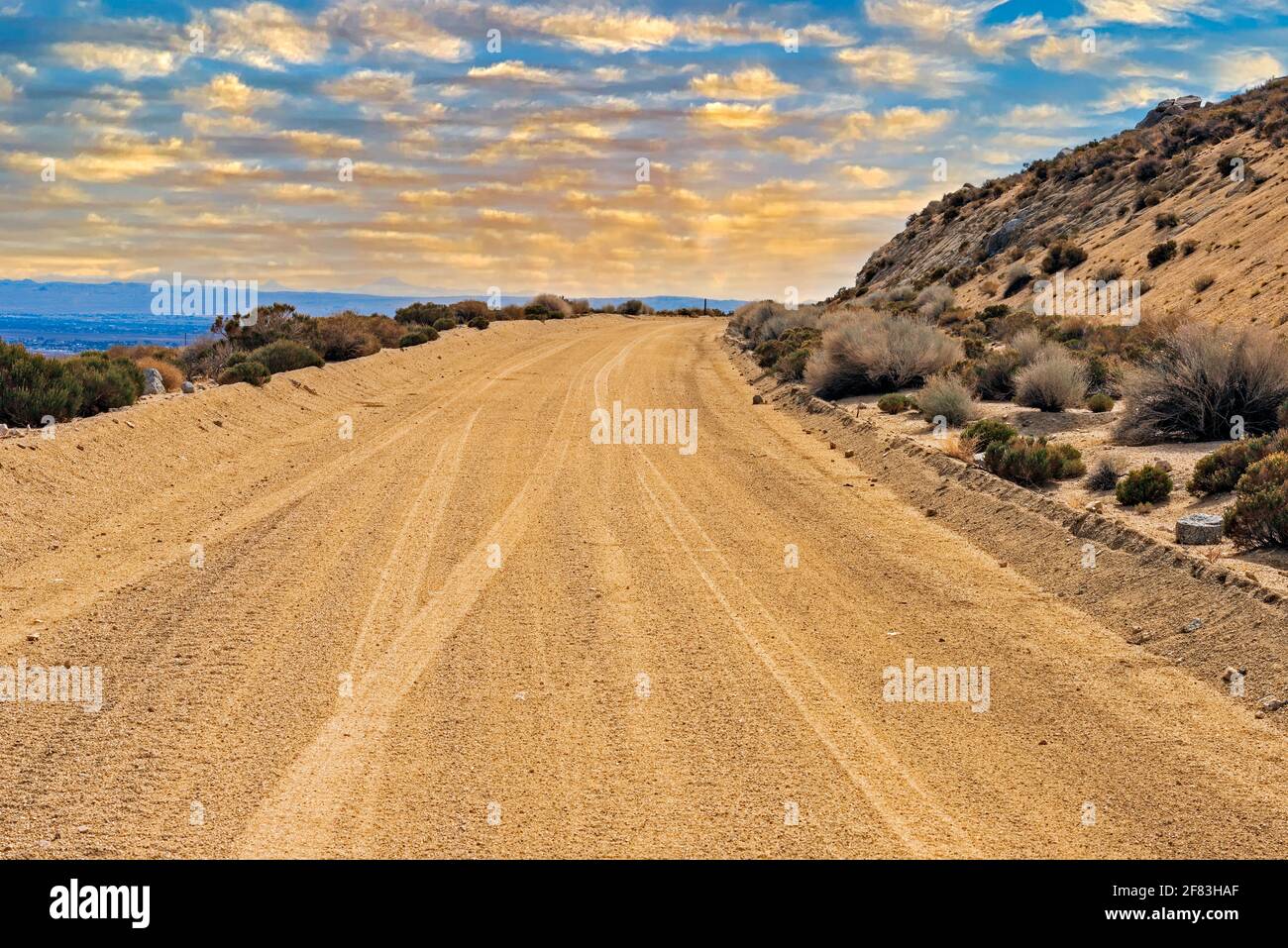 Nuvole gialle d'oro nei cieli blu sopra la solitaria strada sterrata del deserto che conduce verso l'orizzonte. Foto Stock