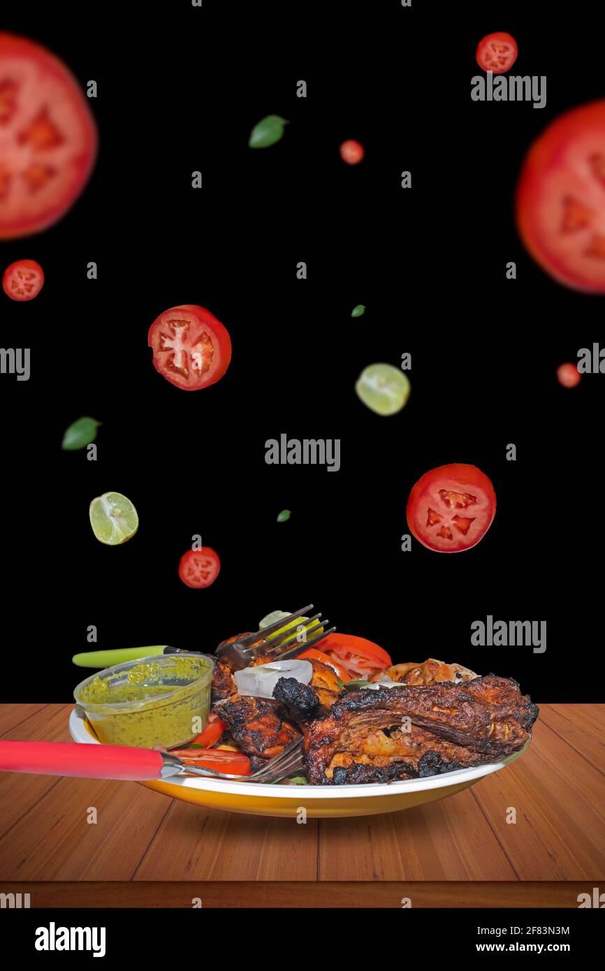 Piatto piccante fatto in casa pollo tandoori con pomodori, limone e piccante volare su uno sfondo scuro Foto Stock