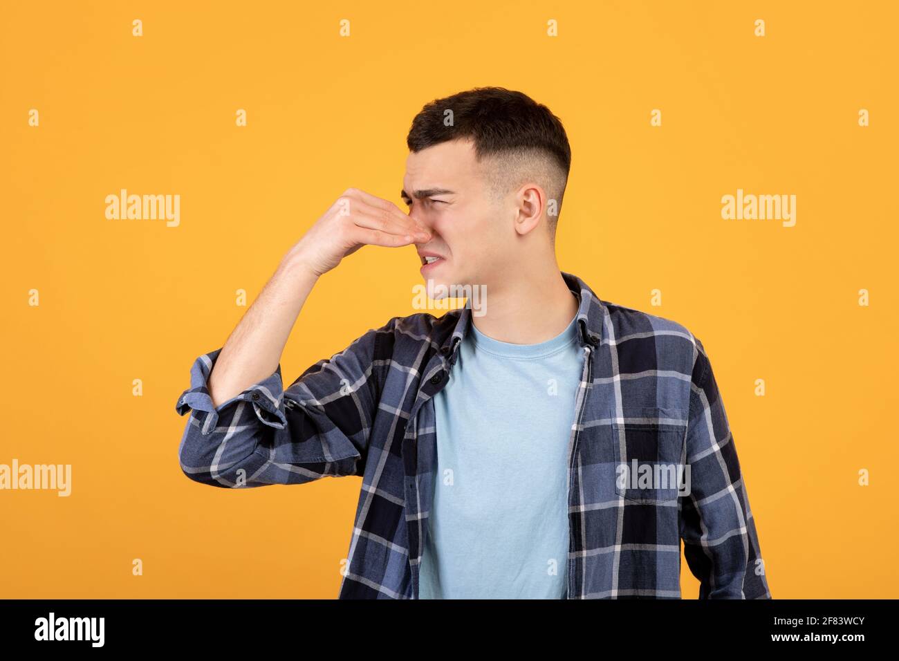 Ragazzo fresco millennial che chiude il naso, soffre di odore terribile, sgradisce cattivo odore su sfondo arancione studio Foto Stock