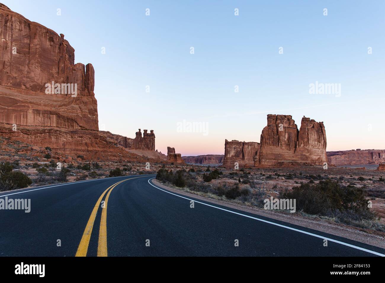 Strada asfaltata con due linee gialle al centro di un canyon di roccia rossa in estate su un'alba Foto Stock