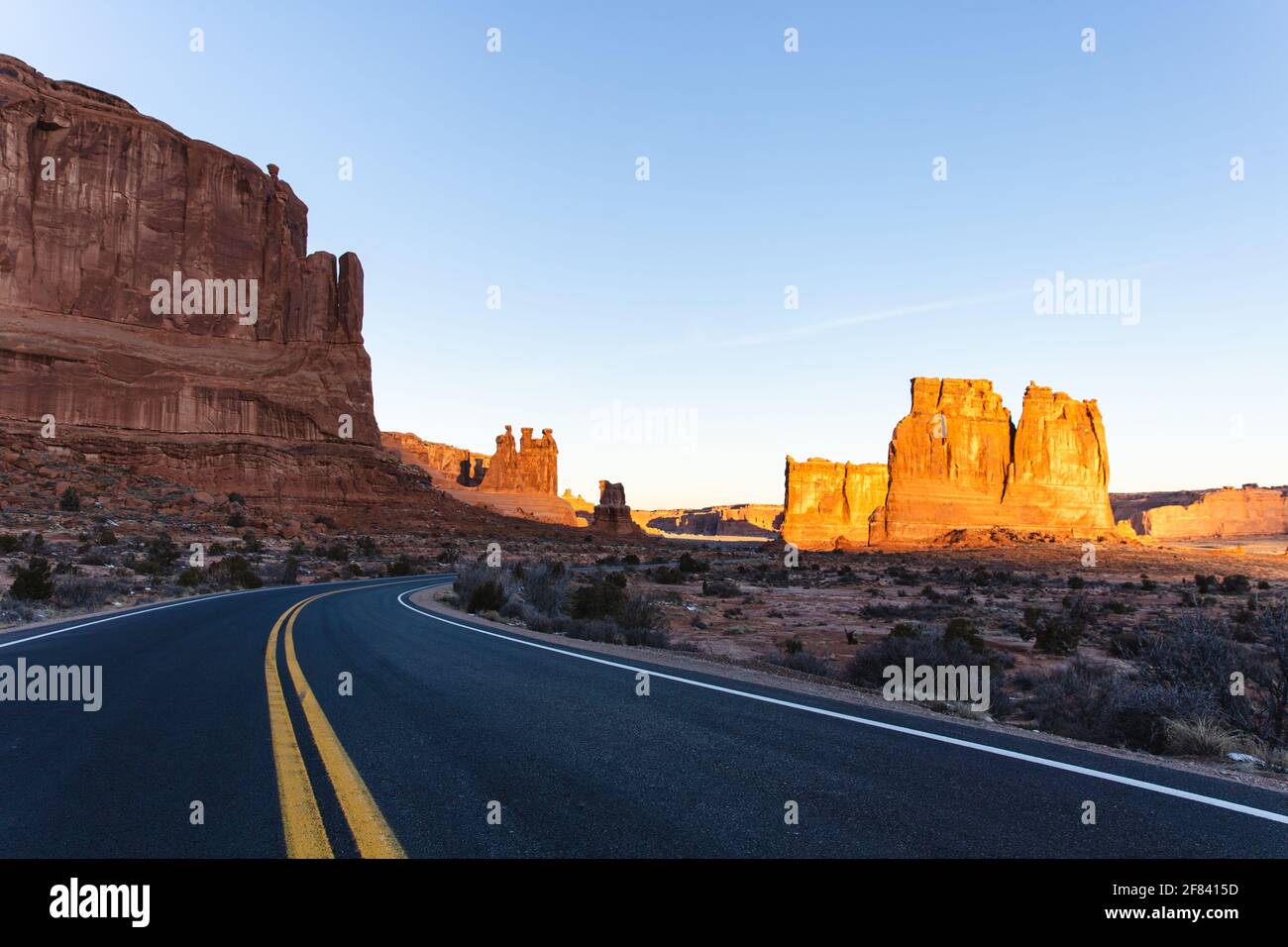 Strada asfaltata con due linee gialle al centro di un canyon di roccia rossa in estate su un'alba con luce brillante Foto Stock