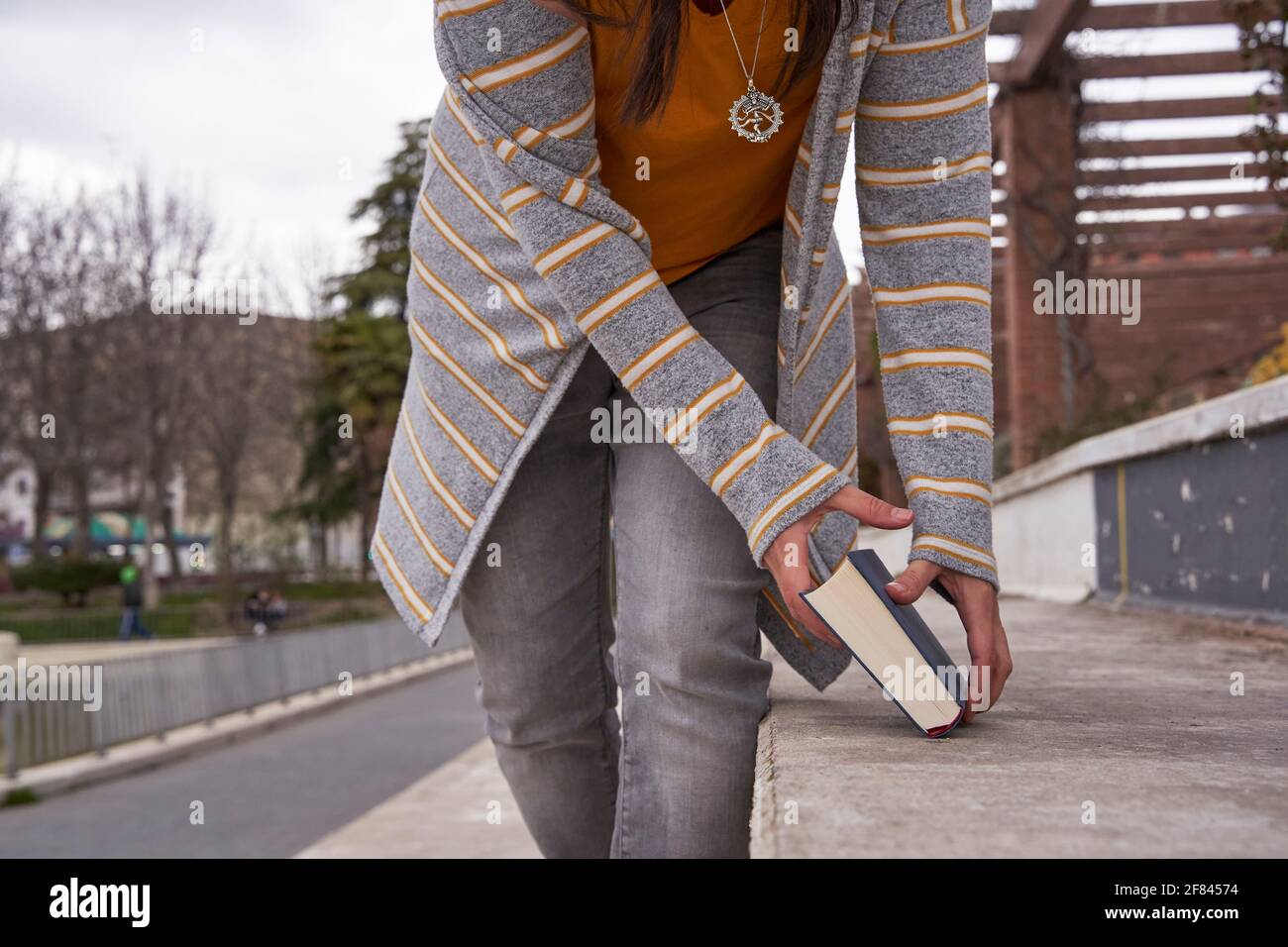 donna tagliata che raccoglie un libro chiuso che ha dimenticato sopra un sedile in pietra Foto Stock