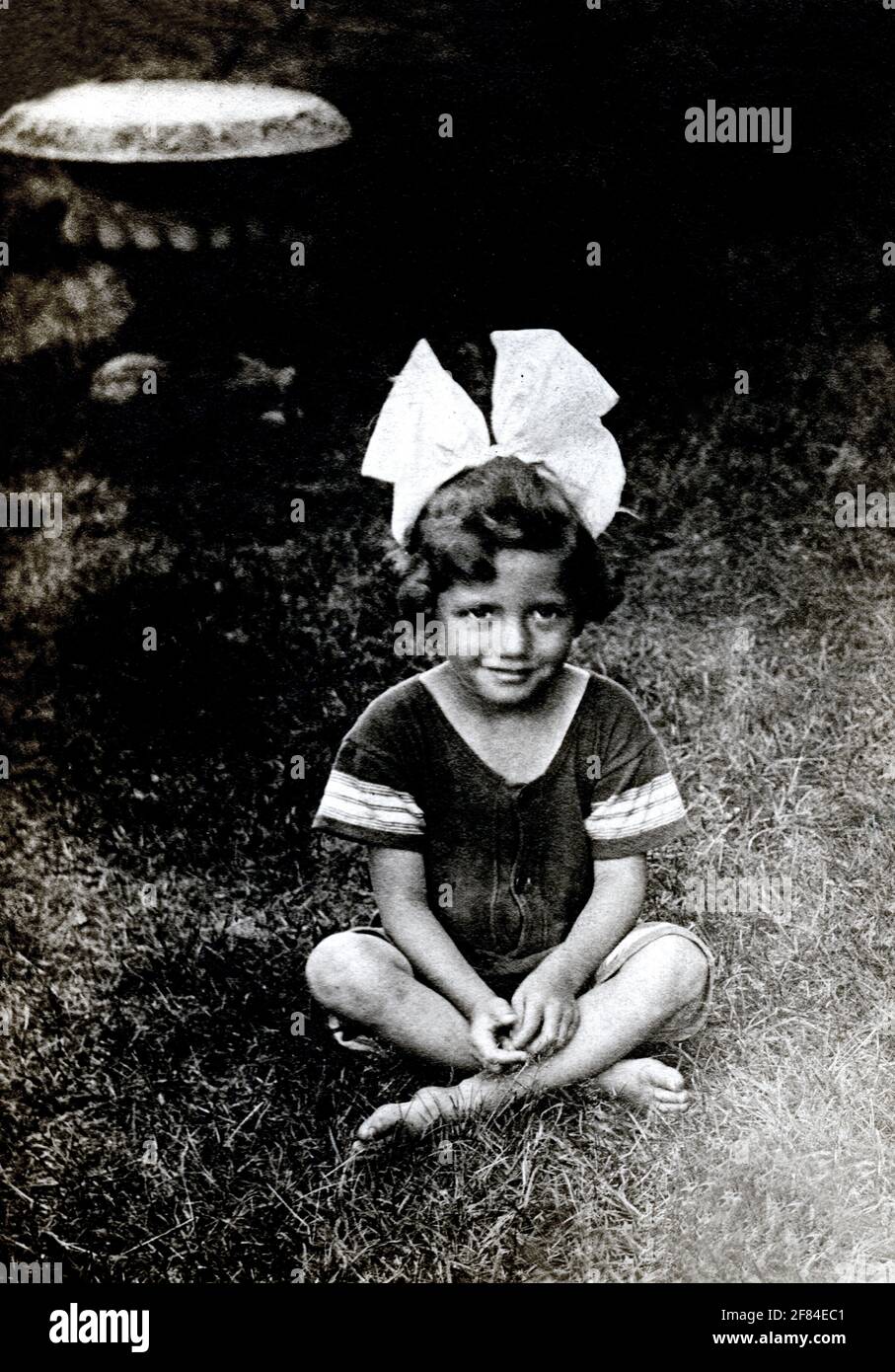 Foto archivistica del 1920 di una bambina seduta all'aperto con un grande arco tra i capelli. Foto Stock