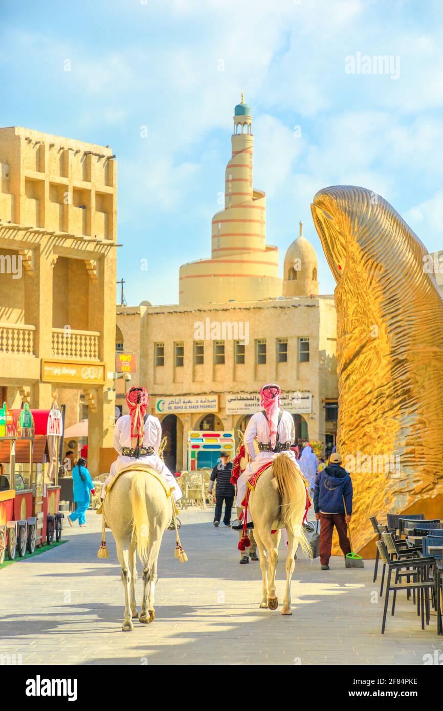 Doha, Qatar - 20 Febbraio 2019: Ufficiali di polizia che cavalcano cavalli arabi bianchi al mercato Souq Waqif. Centro Culturale Islamico di Fanar con Moschea a spirale Foto Stock