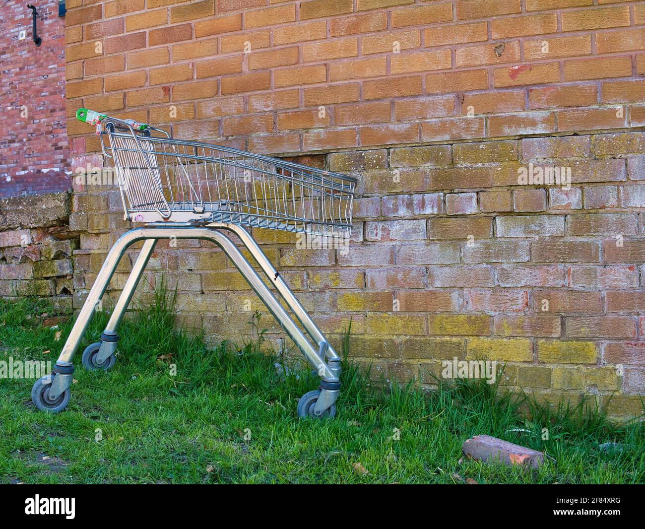 Un carrello per acquisti al supermercato senza marchio, danneggiato, gettato in un'area urbana. Raffigurato contro uno sfondo di un muro di mattoni intemperie. Foto Stock