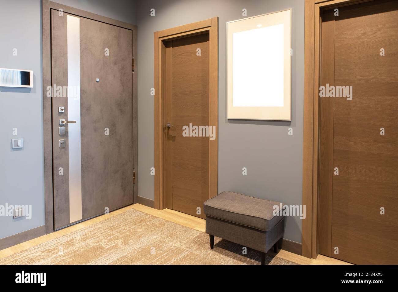 Corridoio d'ingresso moderno in sfumature neutre di marrone e grigio. A parete c'è cornice fotografica con mockup, porta anteriore con interfono. Moda concettuale Foto Stock